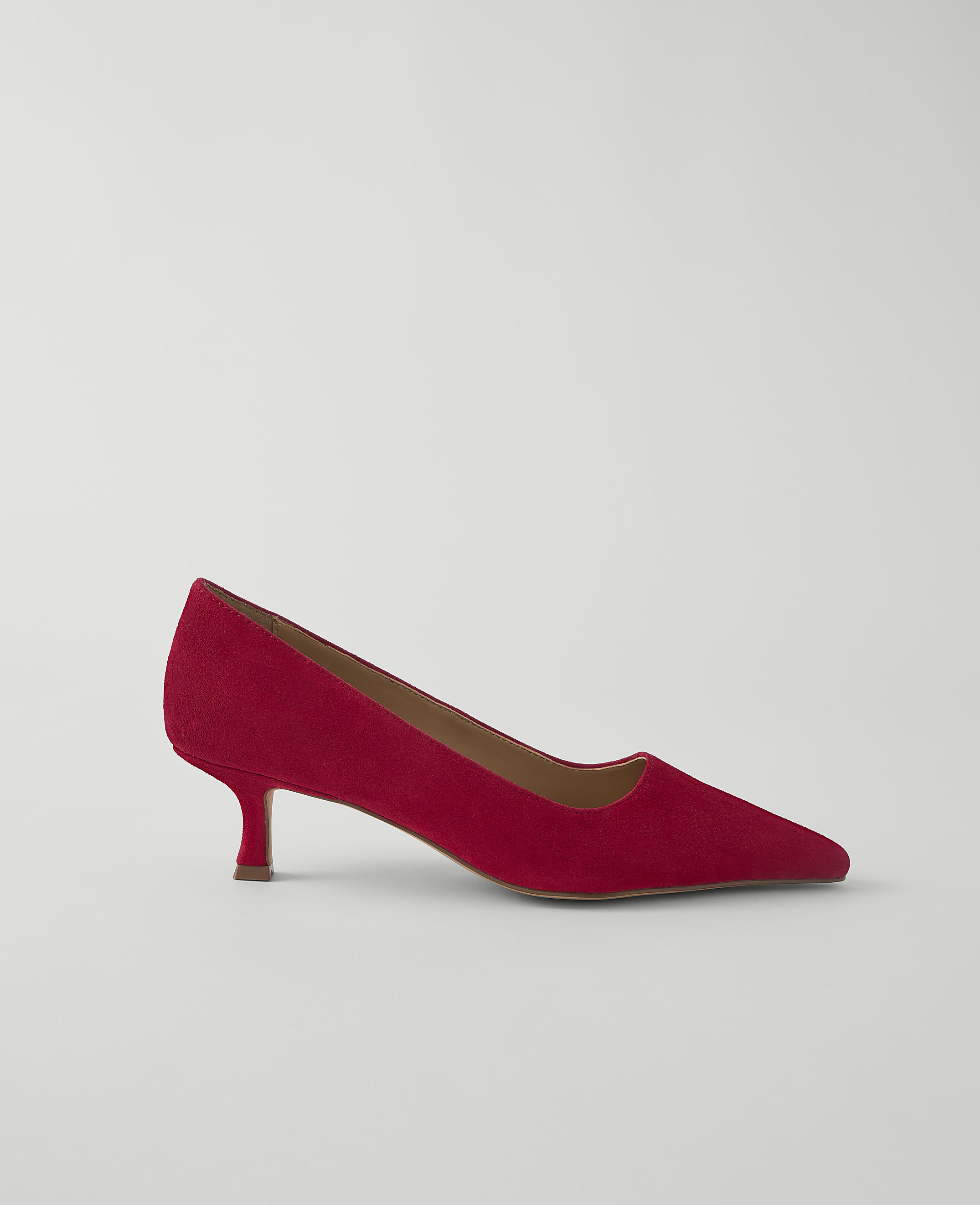 A red suede kitten heel pump rests on a plain white background.