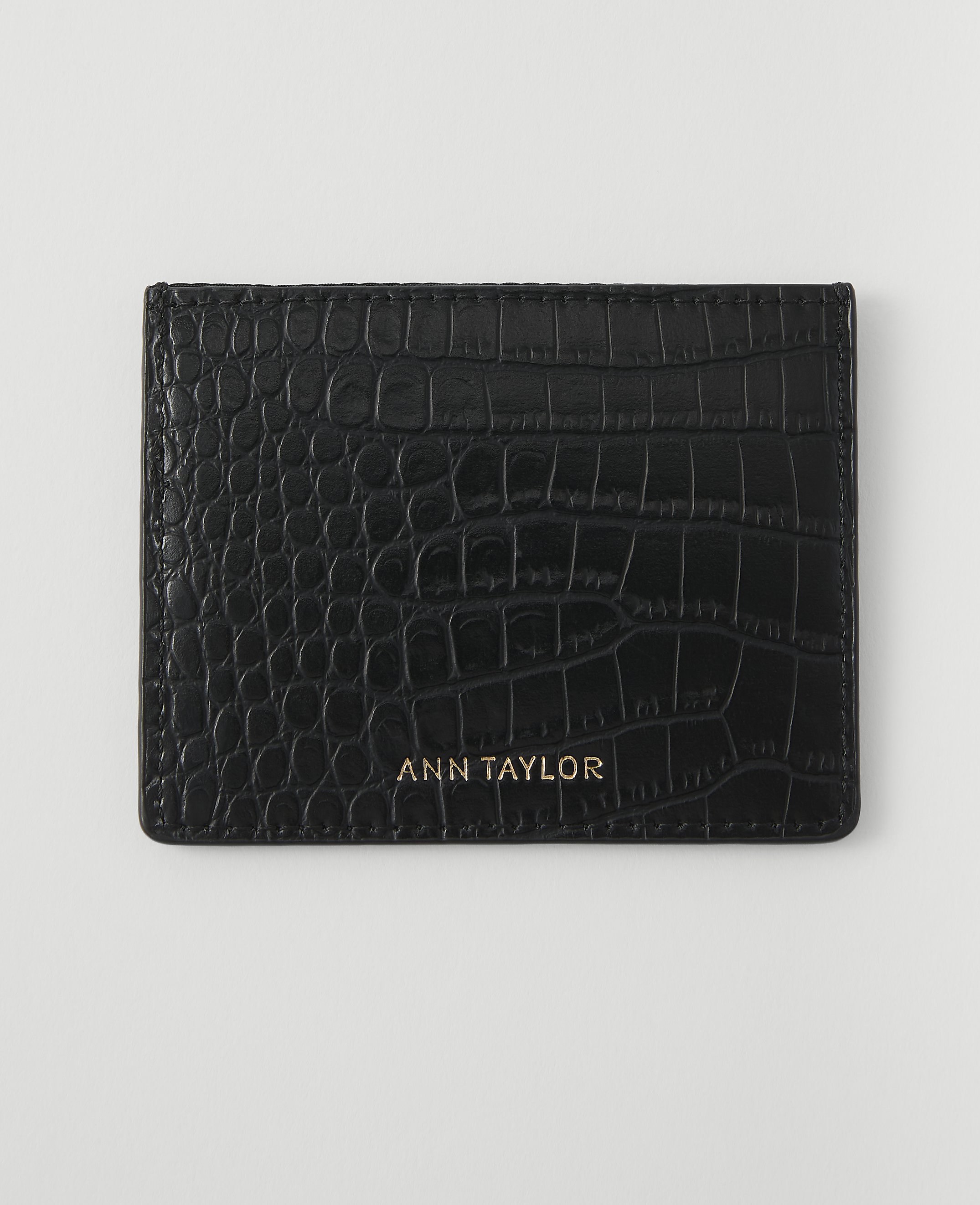 A black, crocodile-embossed cardholder with "ANN TAYLOR" in gold lettering rests on a plain white background.