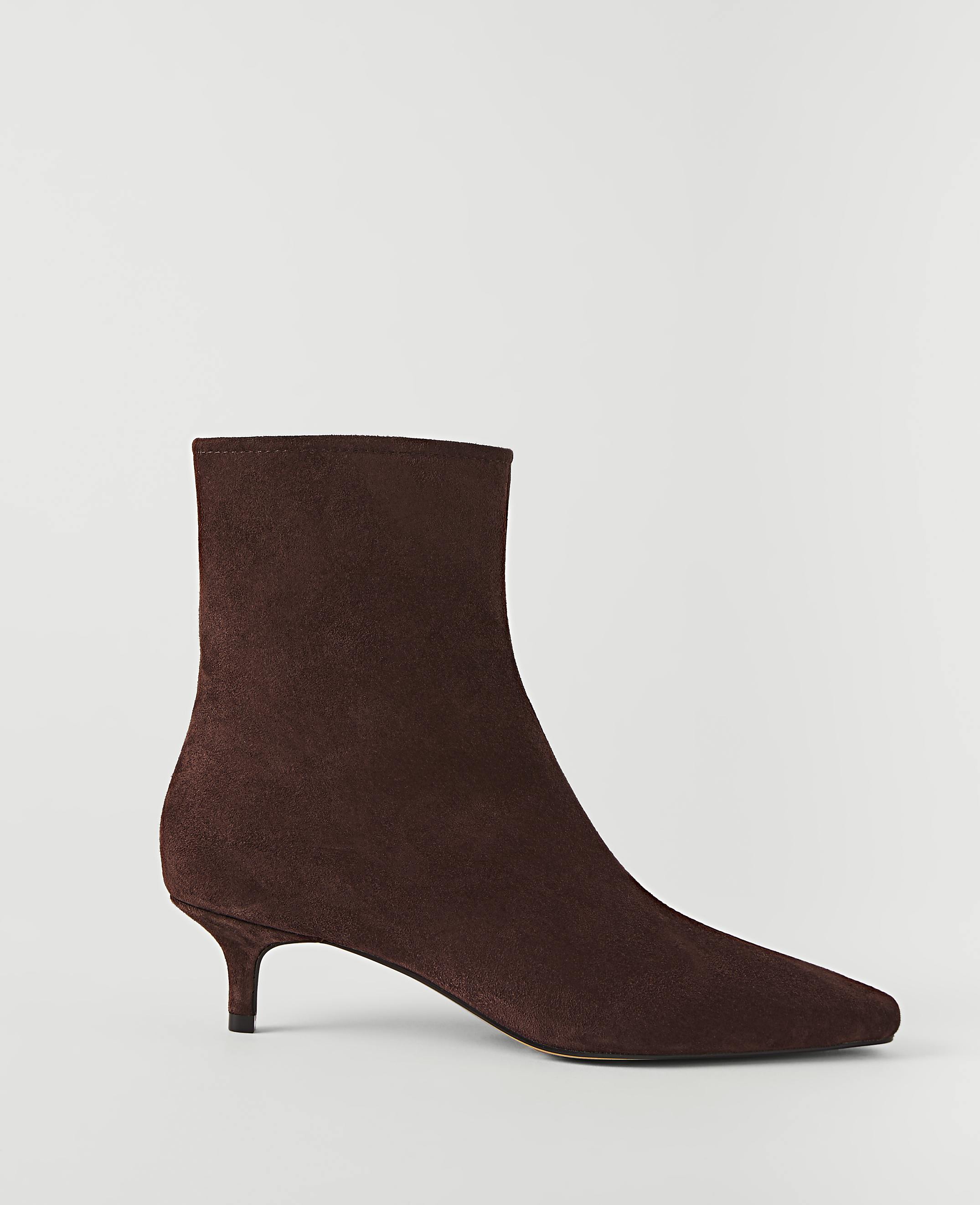 A brown suede ankle boot with a pointed toe and kitten heel stands against a plain white background.