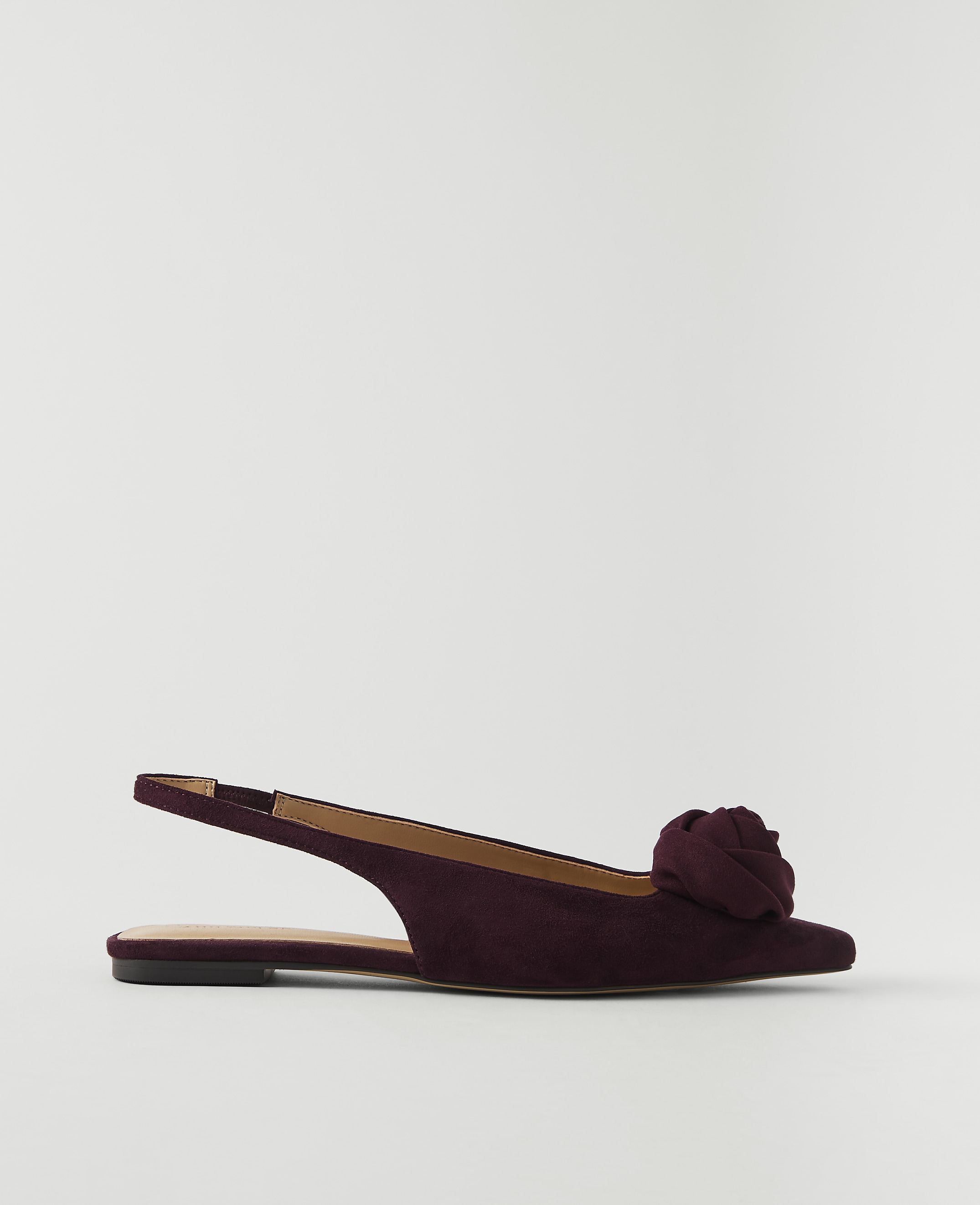 A deep red suede slingback flat with a floral embellishment rests on a plain white background.