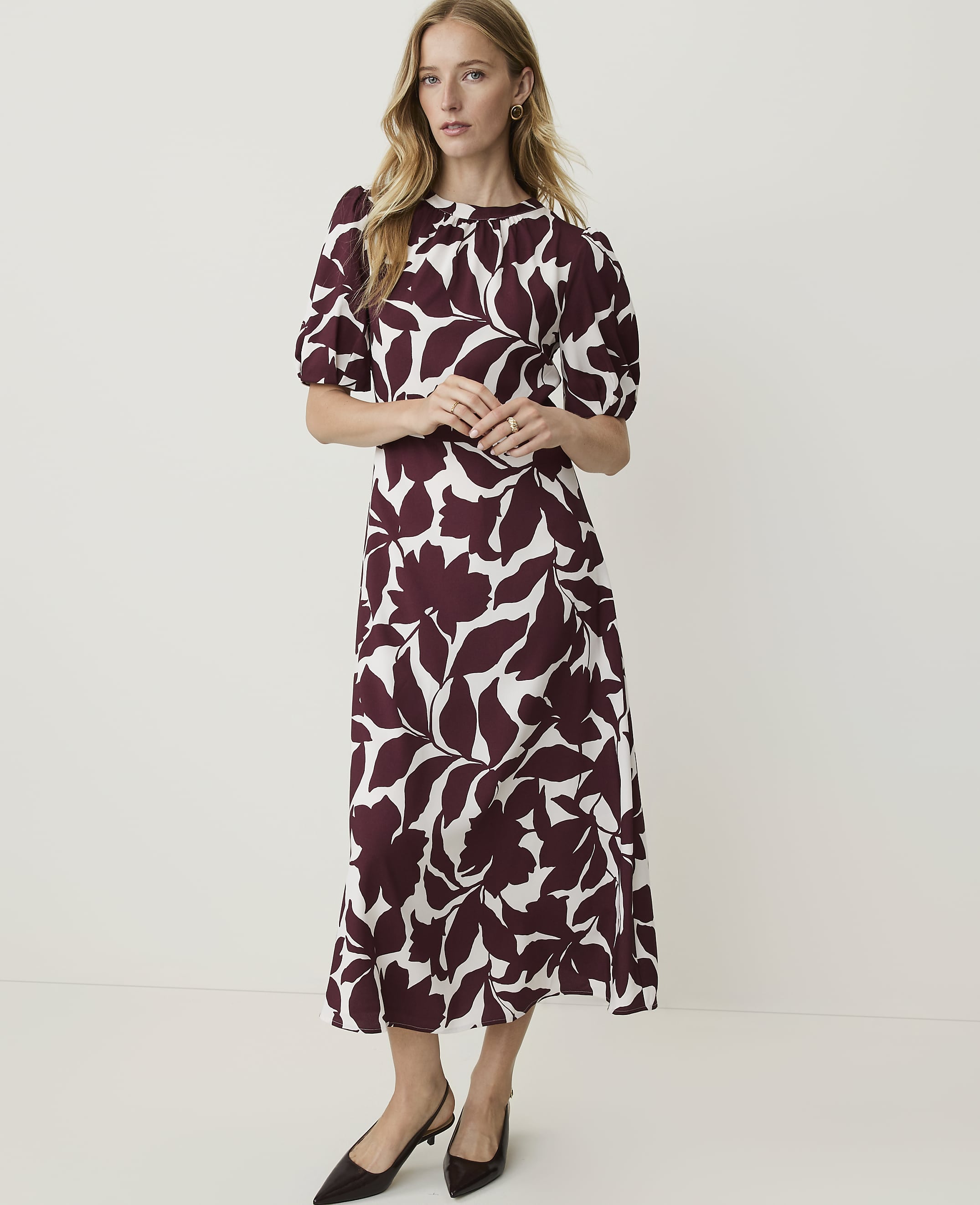 A woman in a floral dress stands against a plain white background.