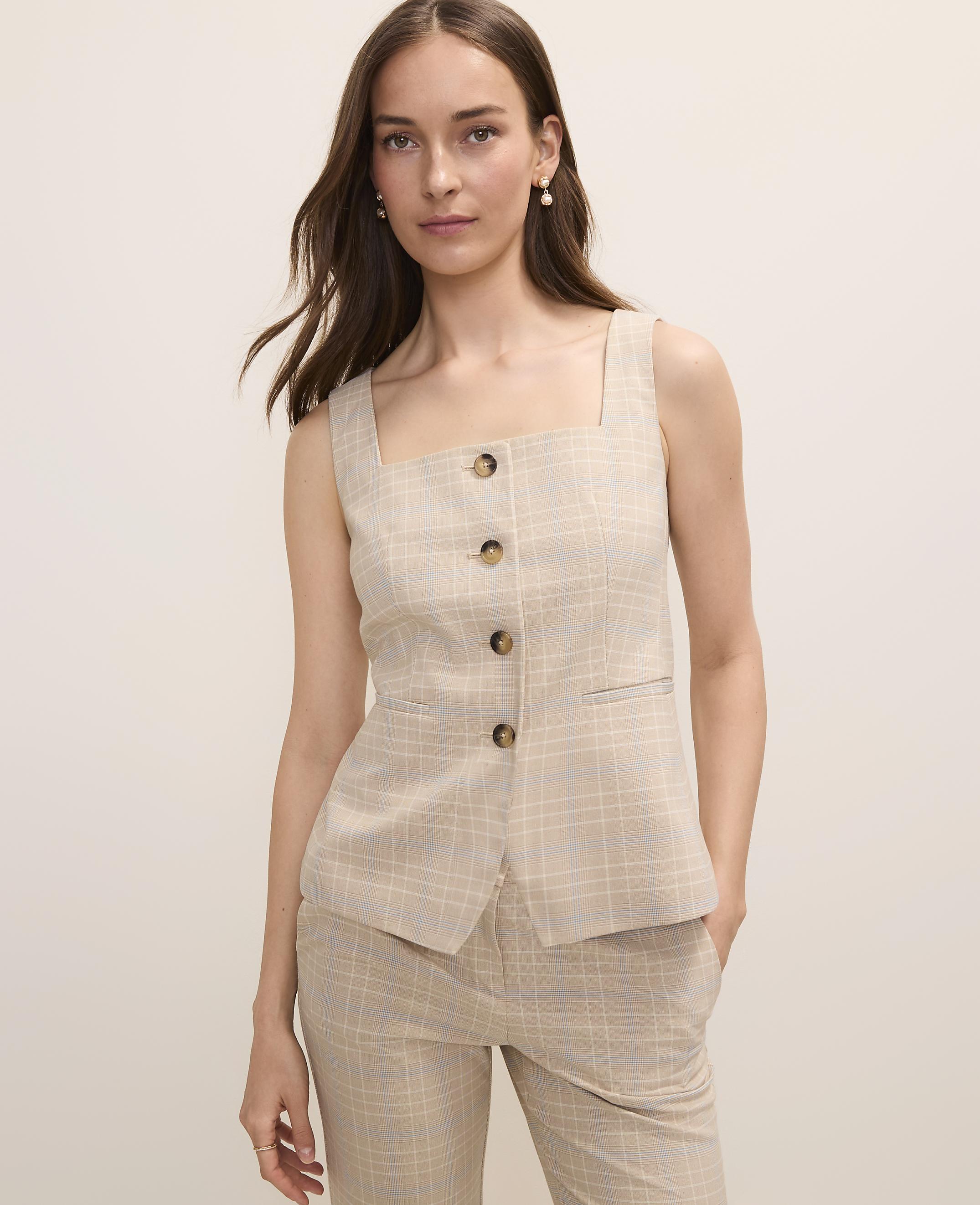 A woman in a plaid vest and pants stands against a plain, light-colored background.