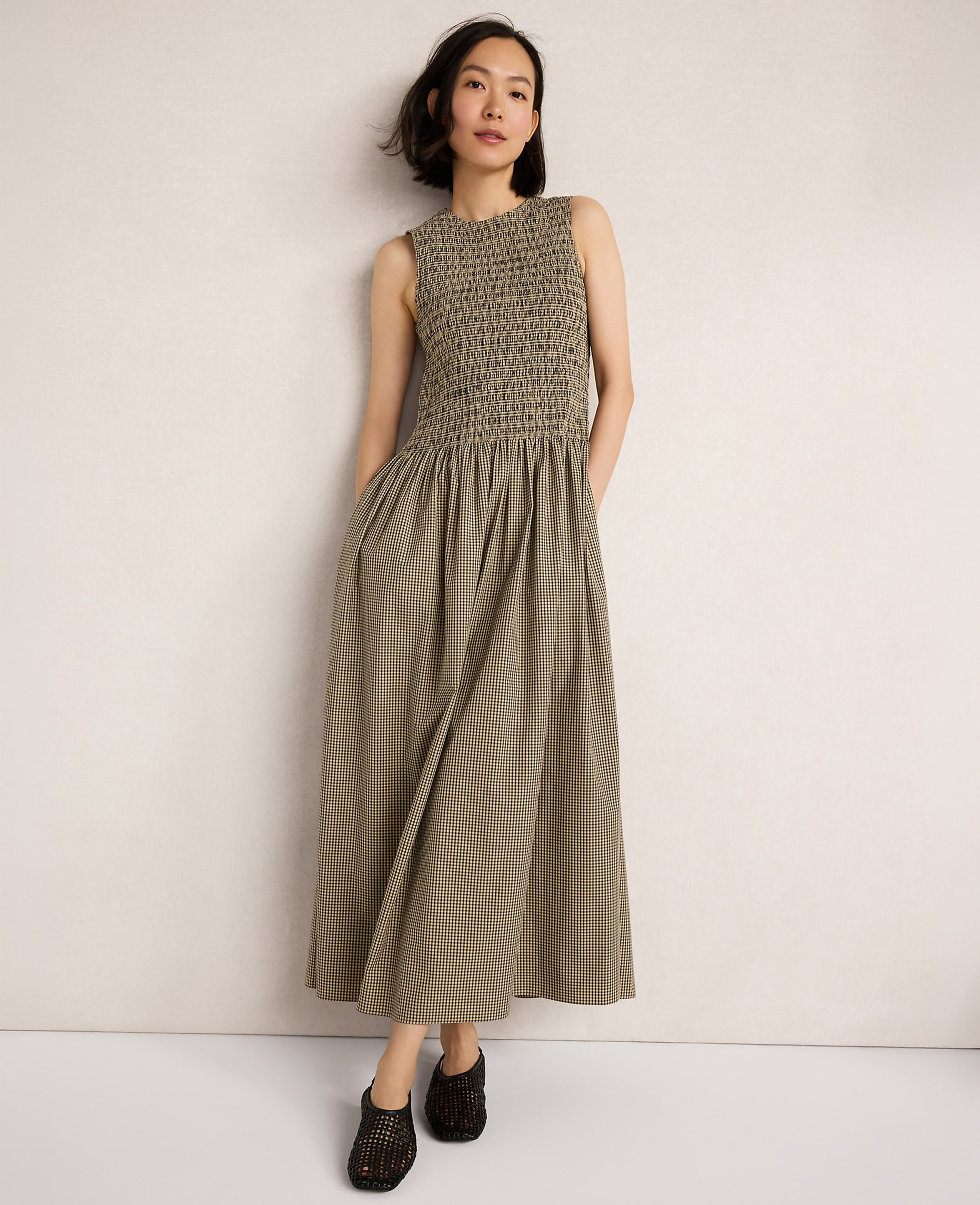 A woman in a smocked olive green dress stands against a plain, light-colored wall.