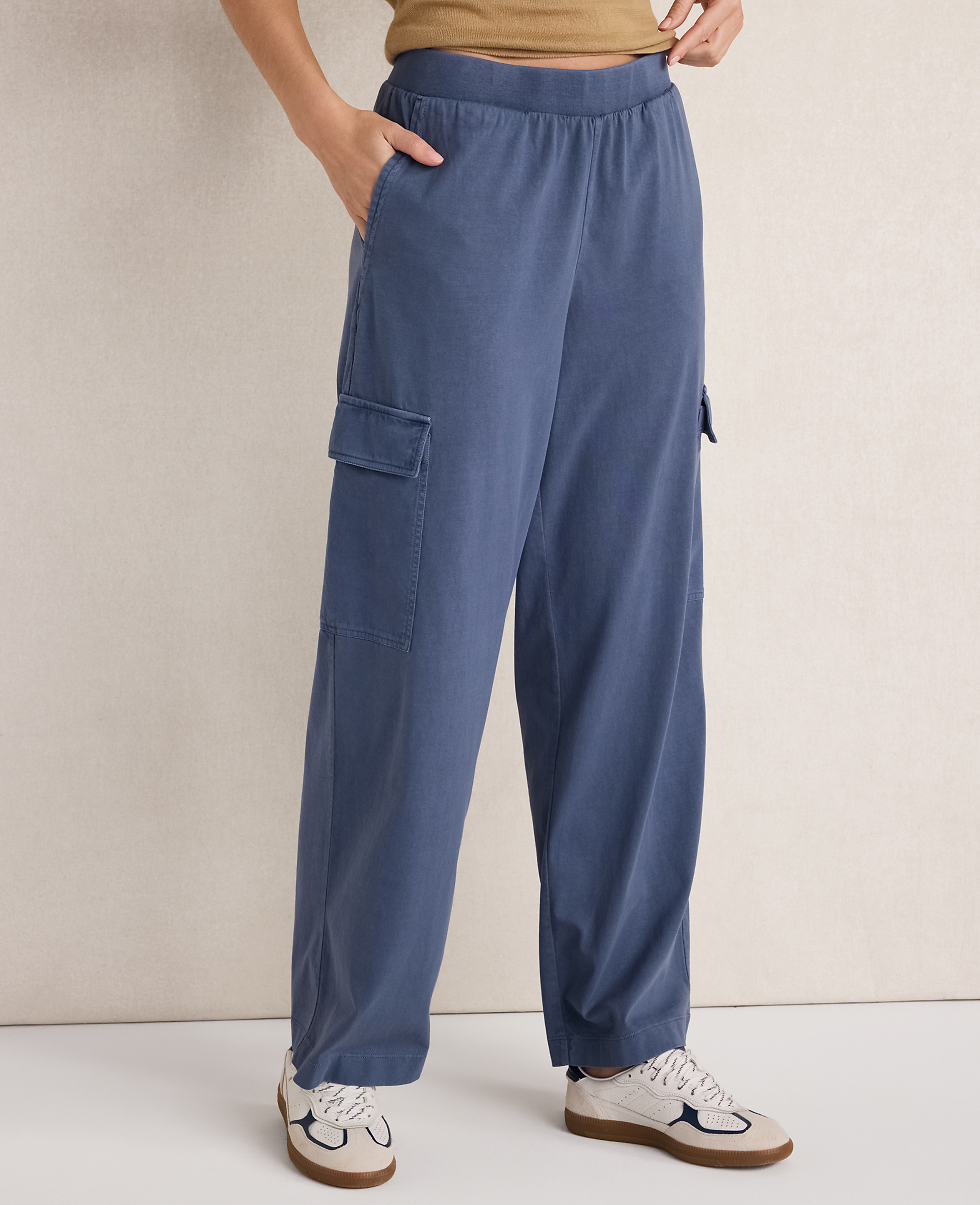 A person stands in loose-fitting blue cargo pants and white sneakers against a plain, light-colored background.