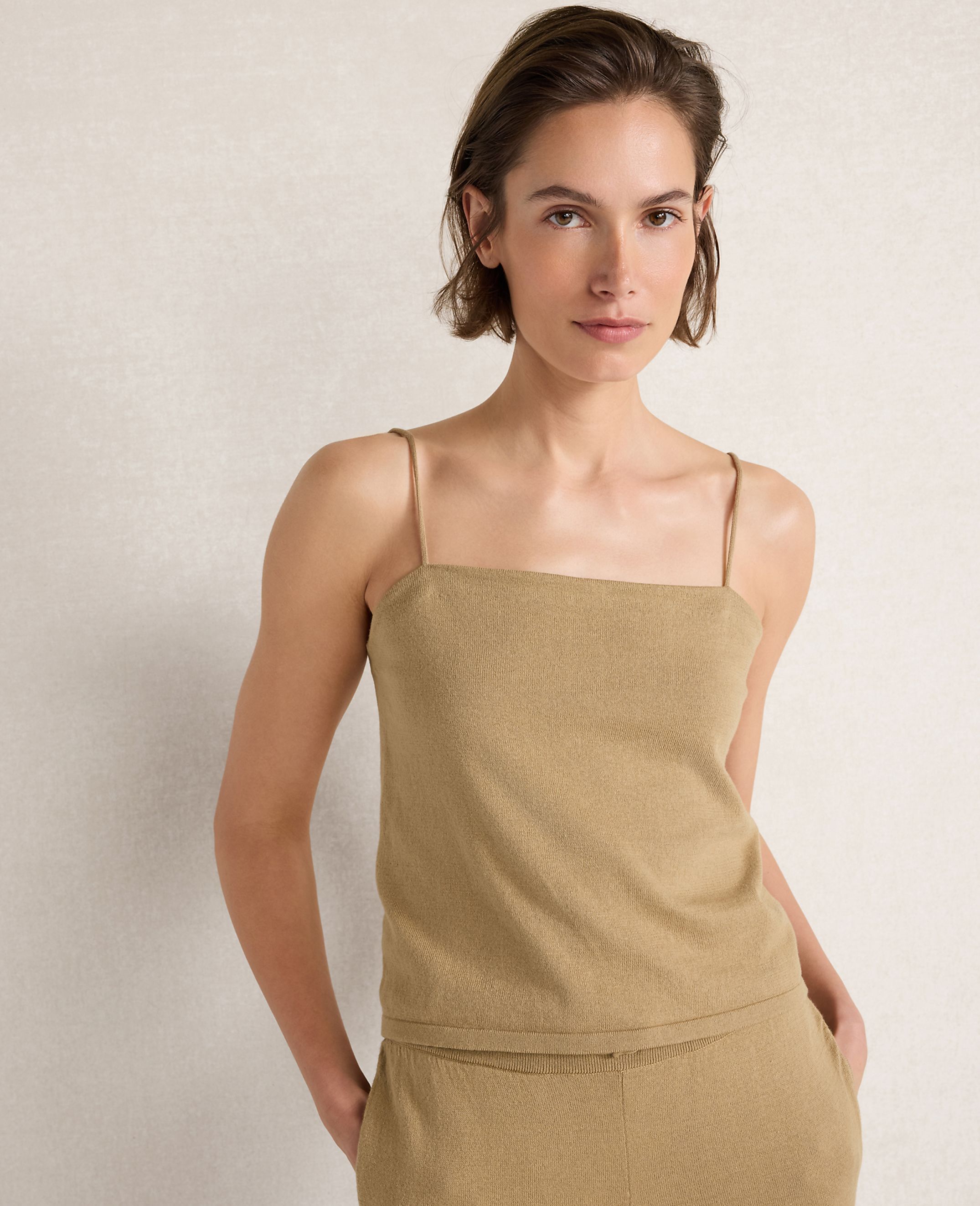 A woman in a tan camisole stands against a textured, light-colored background.