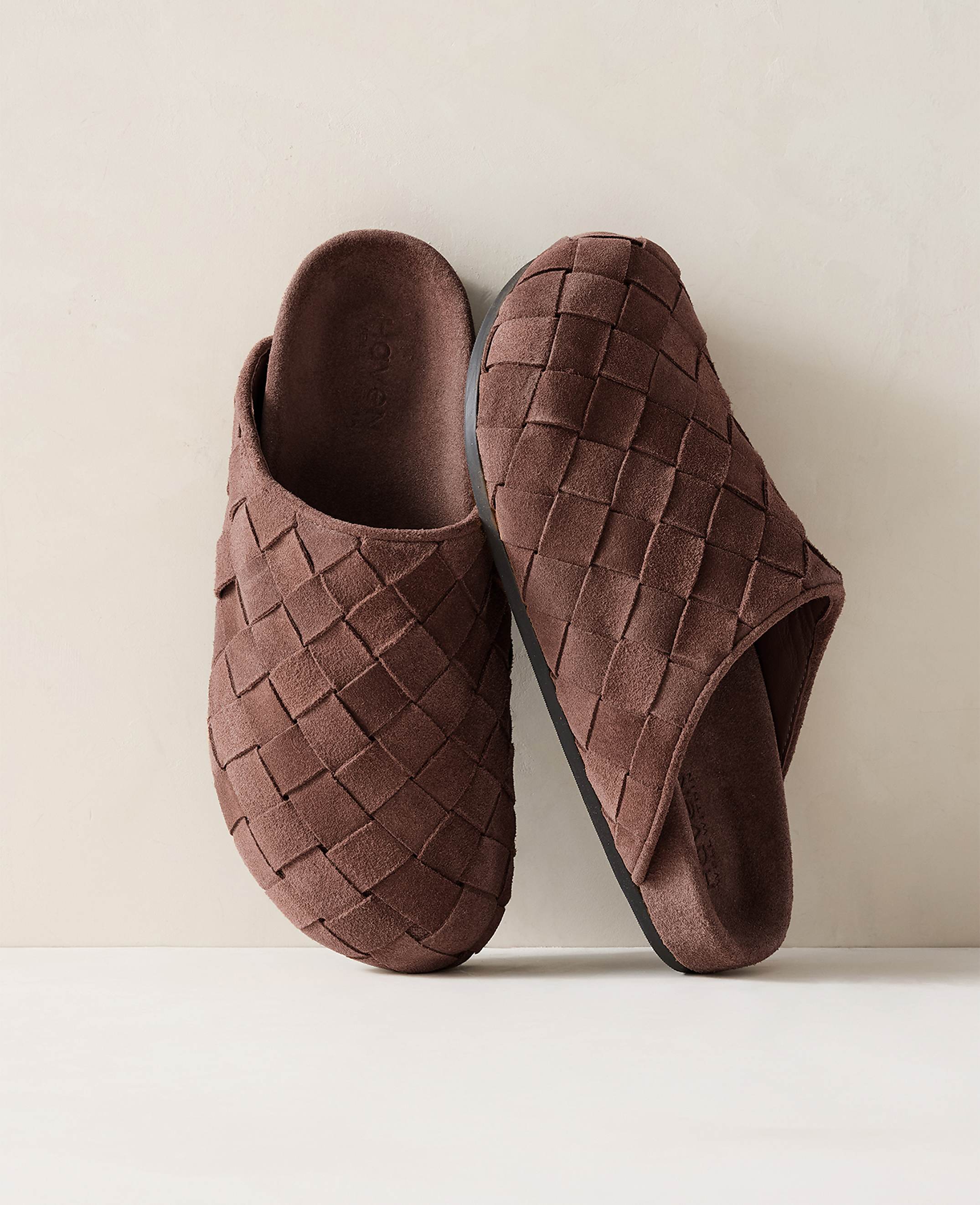 A pair of brown woven slippers rests on a light-colored surface against a soft, neutral background.