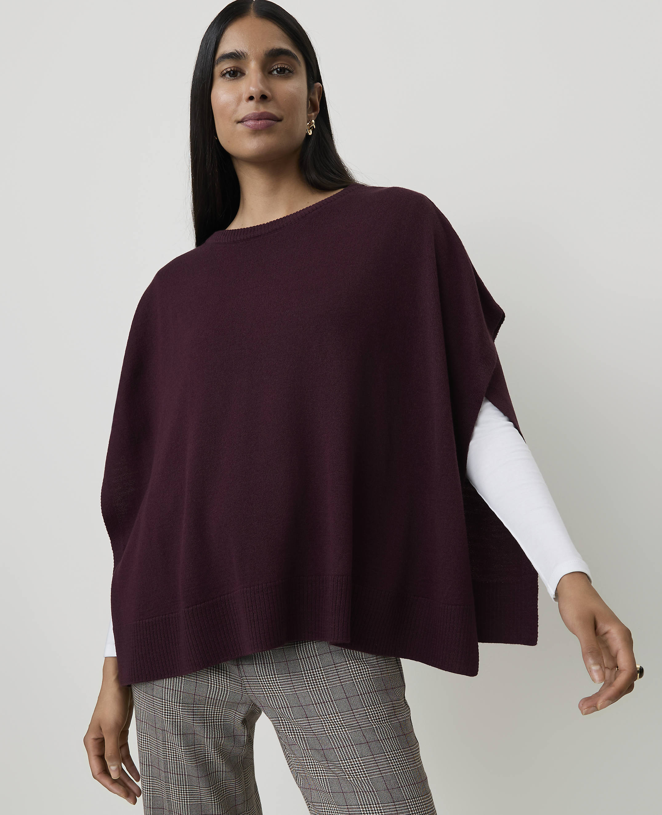 A woman in a maroon poncho and plaid pants stands against a plain white background.