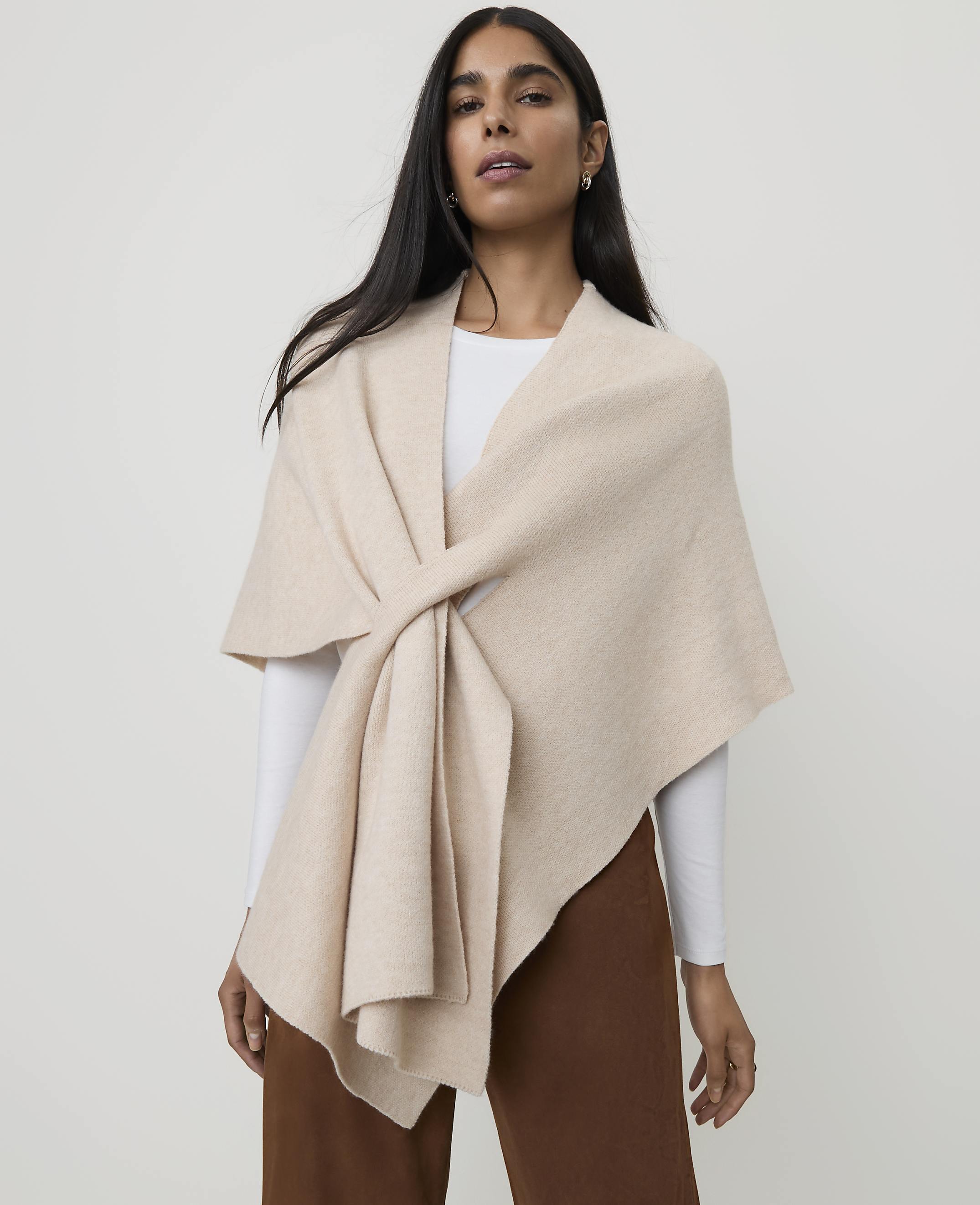 A woman in a cream-colored wrap stands against a plain, light background.