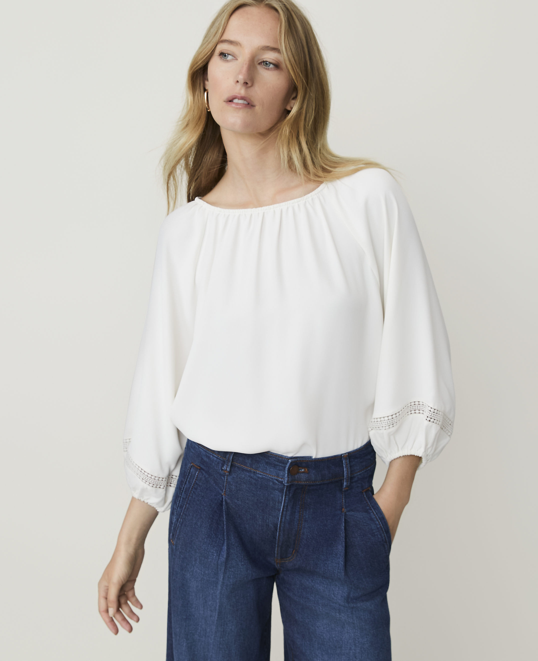 A woman in a white blouse and blue jeans stands against a plain white background.