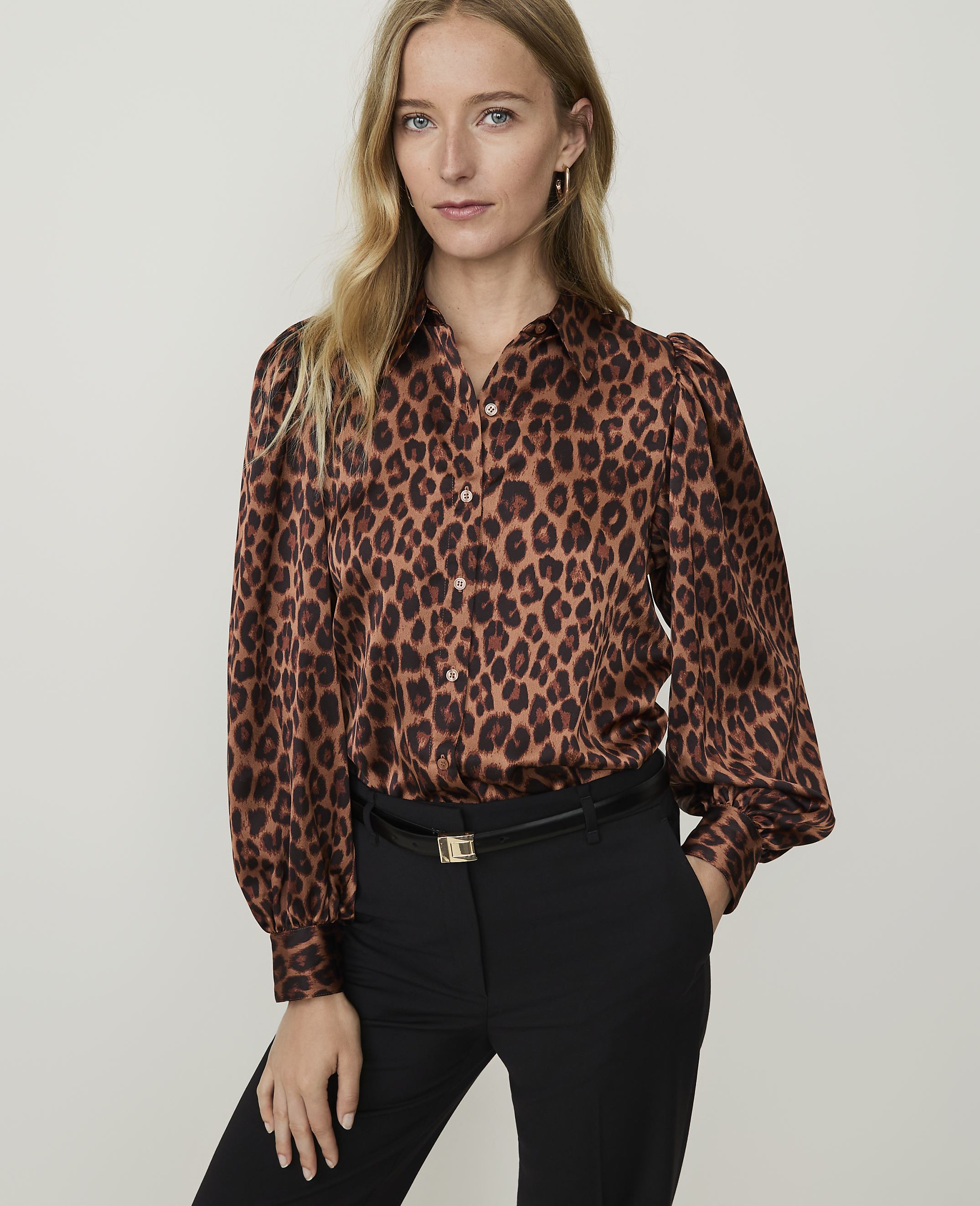 A woman in a leopard print blouse and black pants stands against a plain, light-colored background.