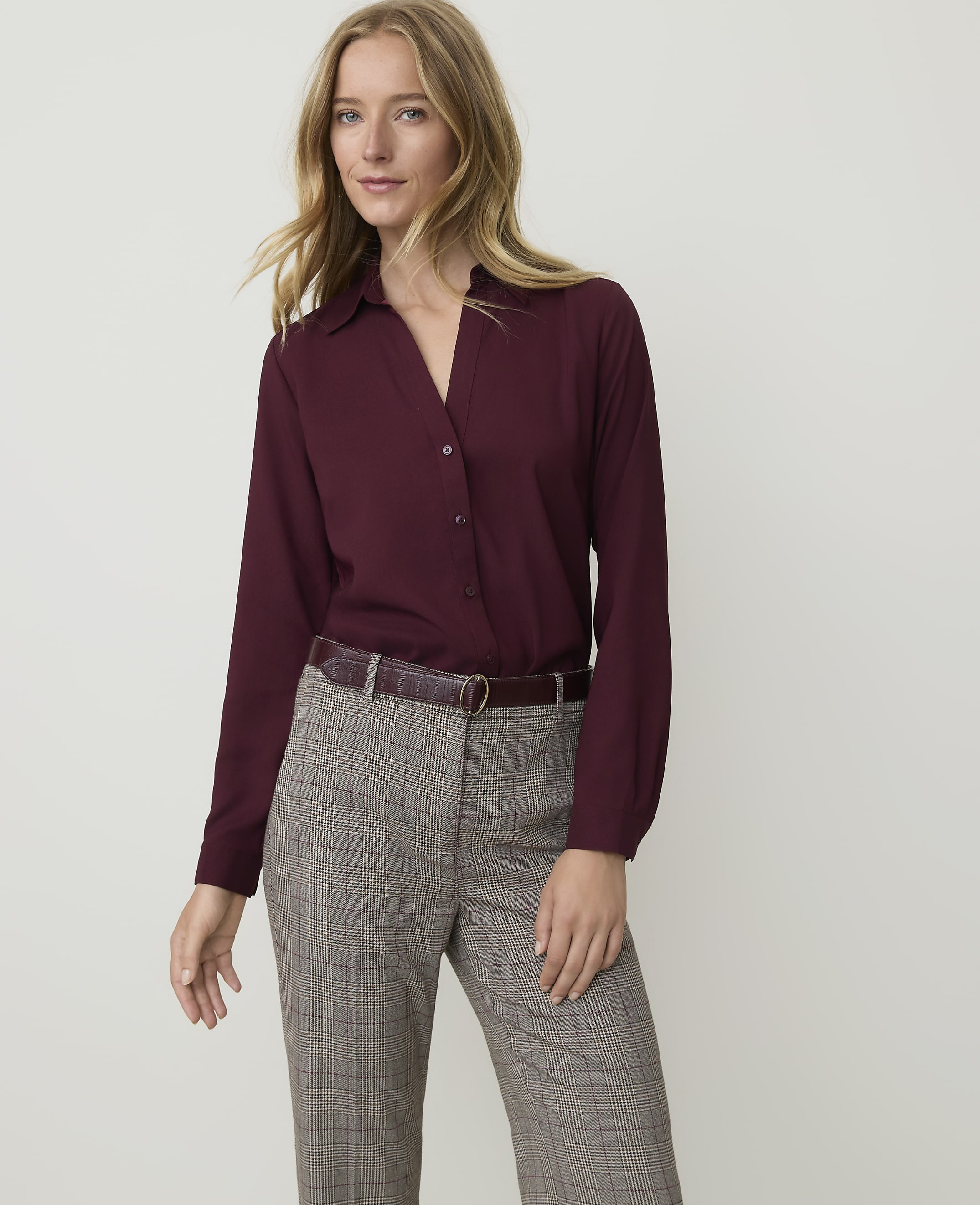 A woman in a burgundy blouse and plaid pants stands against a plain white background.