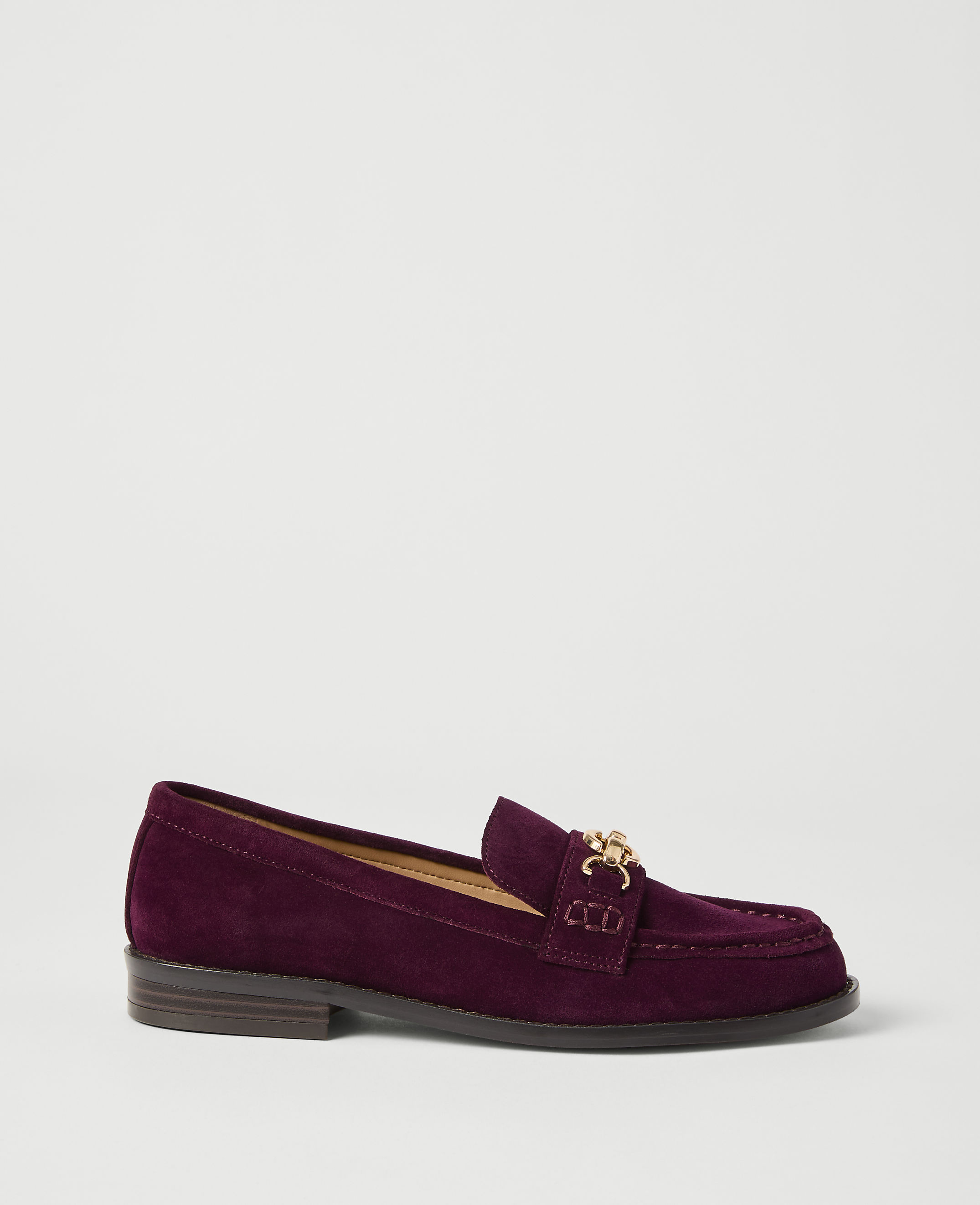 A deep purple suede loafer with a gold chain detail rests on a plain white background.