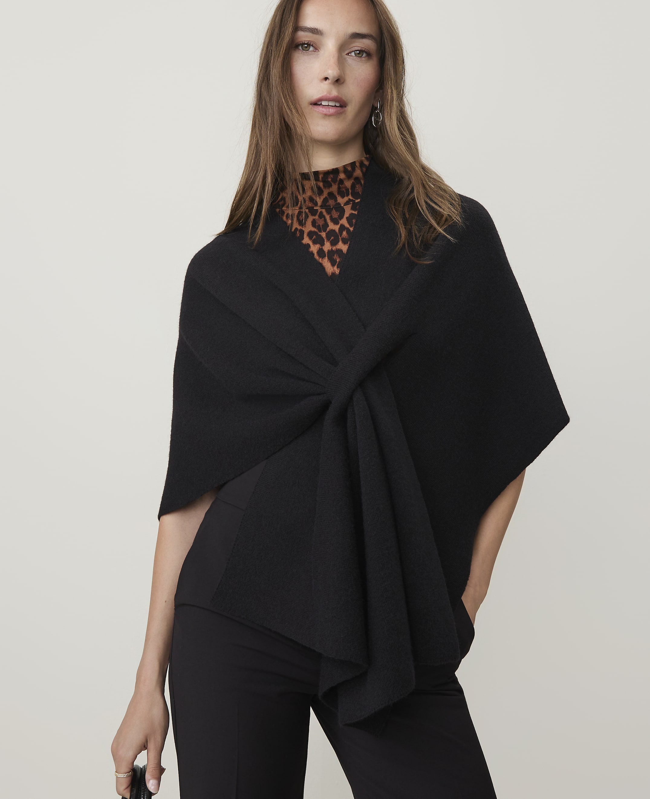A woman in a black wrap and leopard print top stands against a plain background.