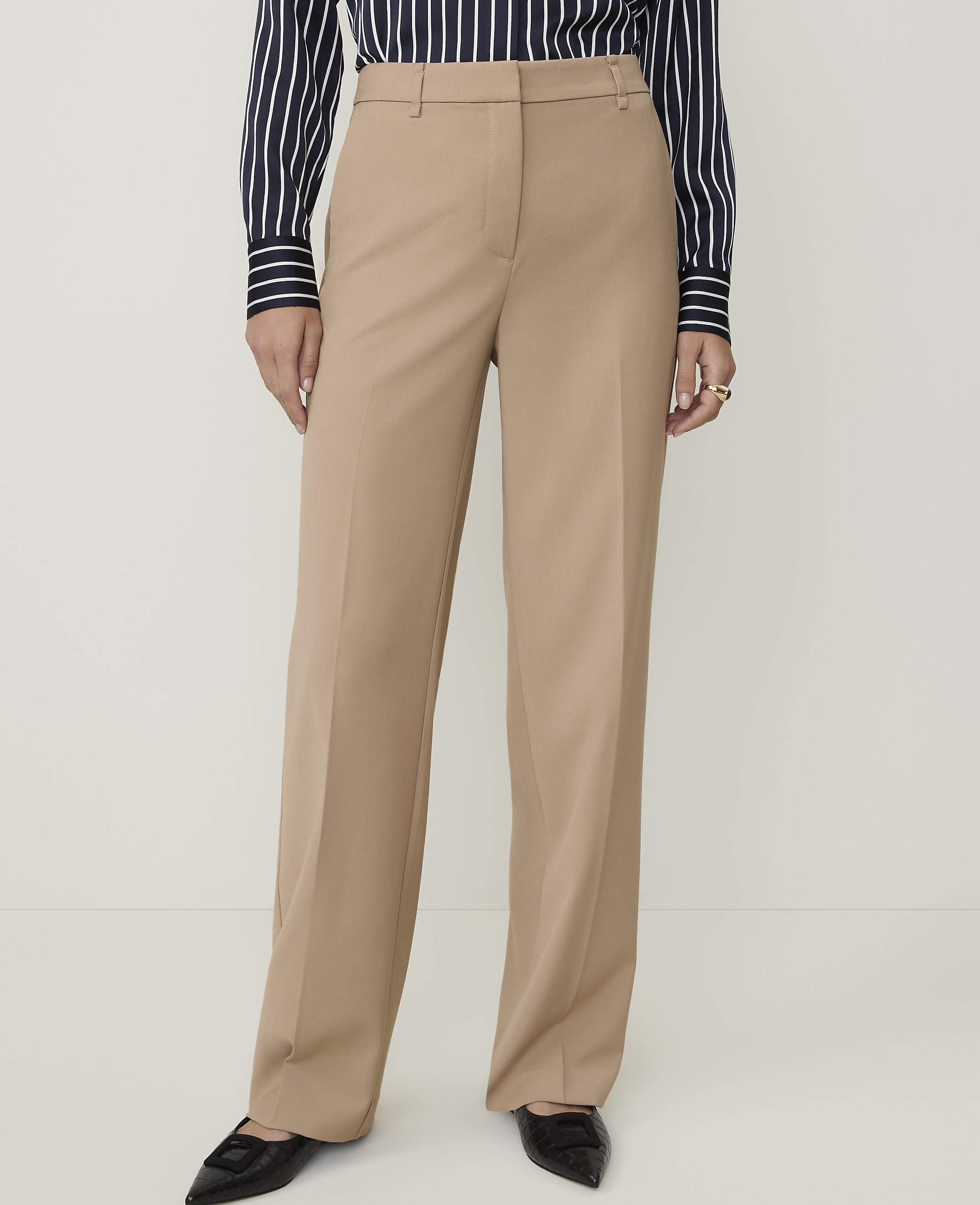A person wearing light-wash, wide-leg jeans and white heeled sandals stands against a plain white background.