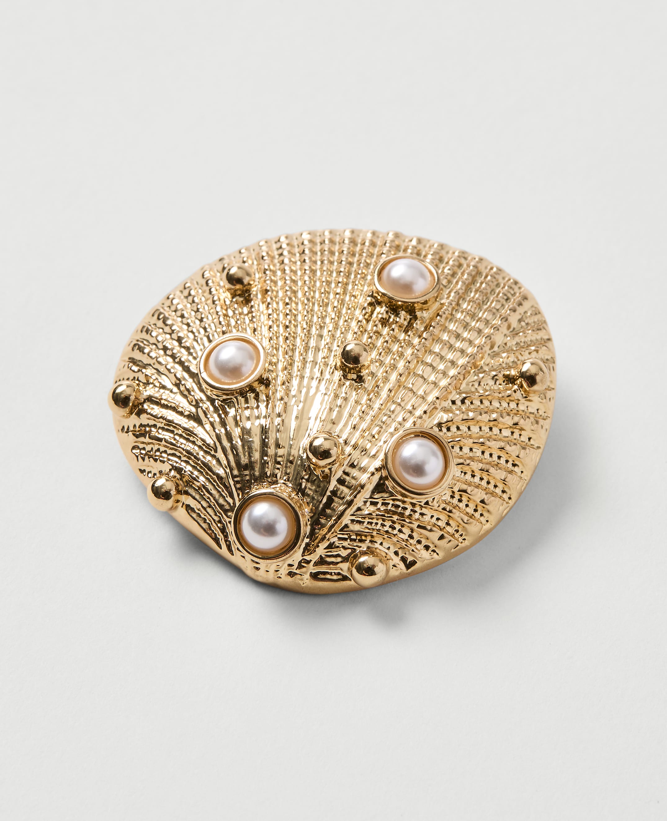A golden seashell brooch with pearls is set against a plain white background.