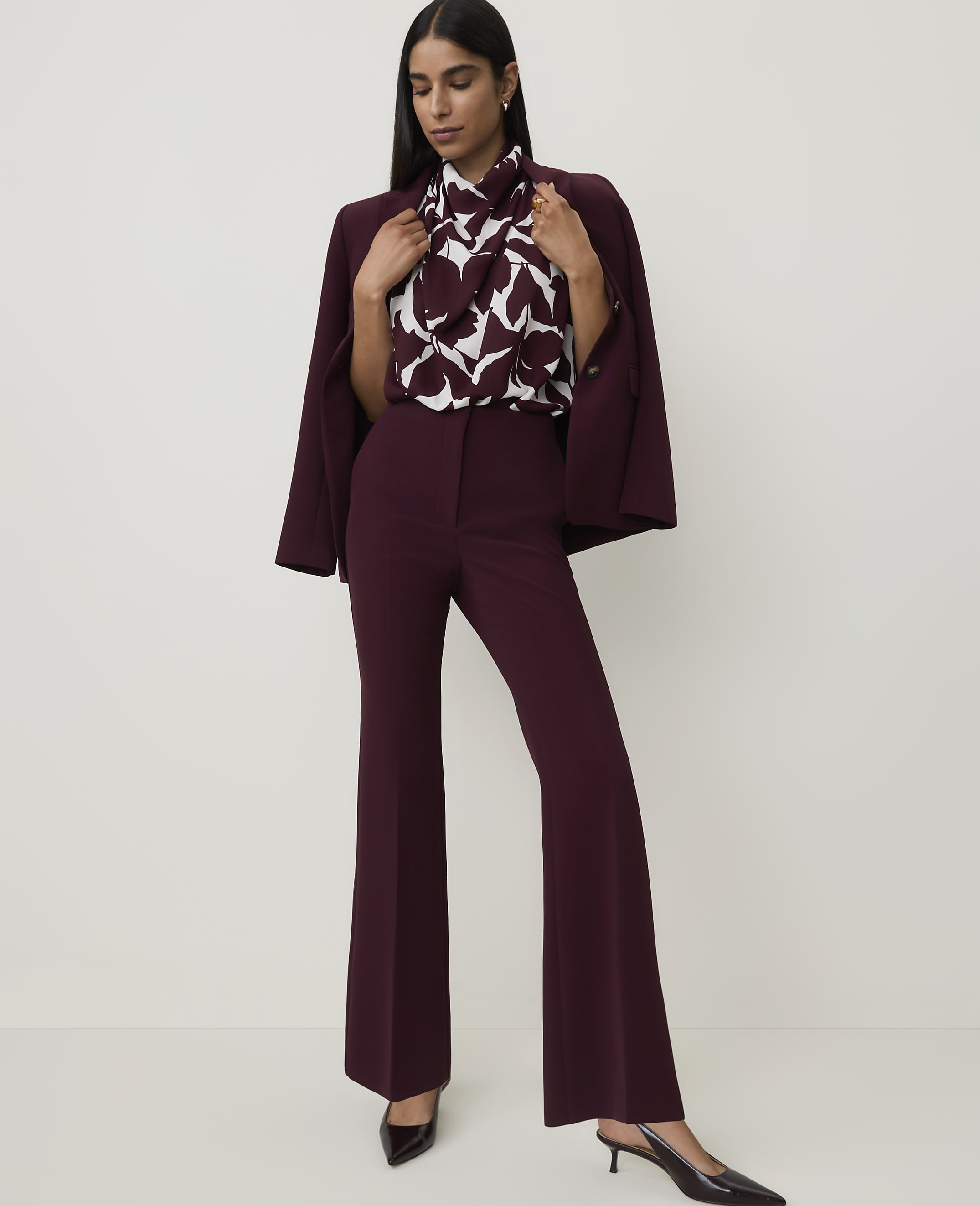 A woman in a burgundy suit with a patterned blouse stands against a plain white background.