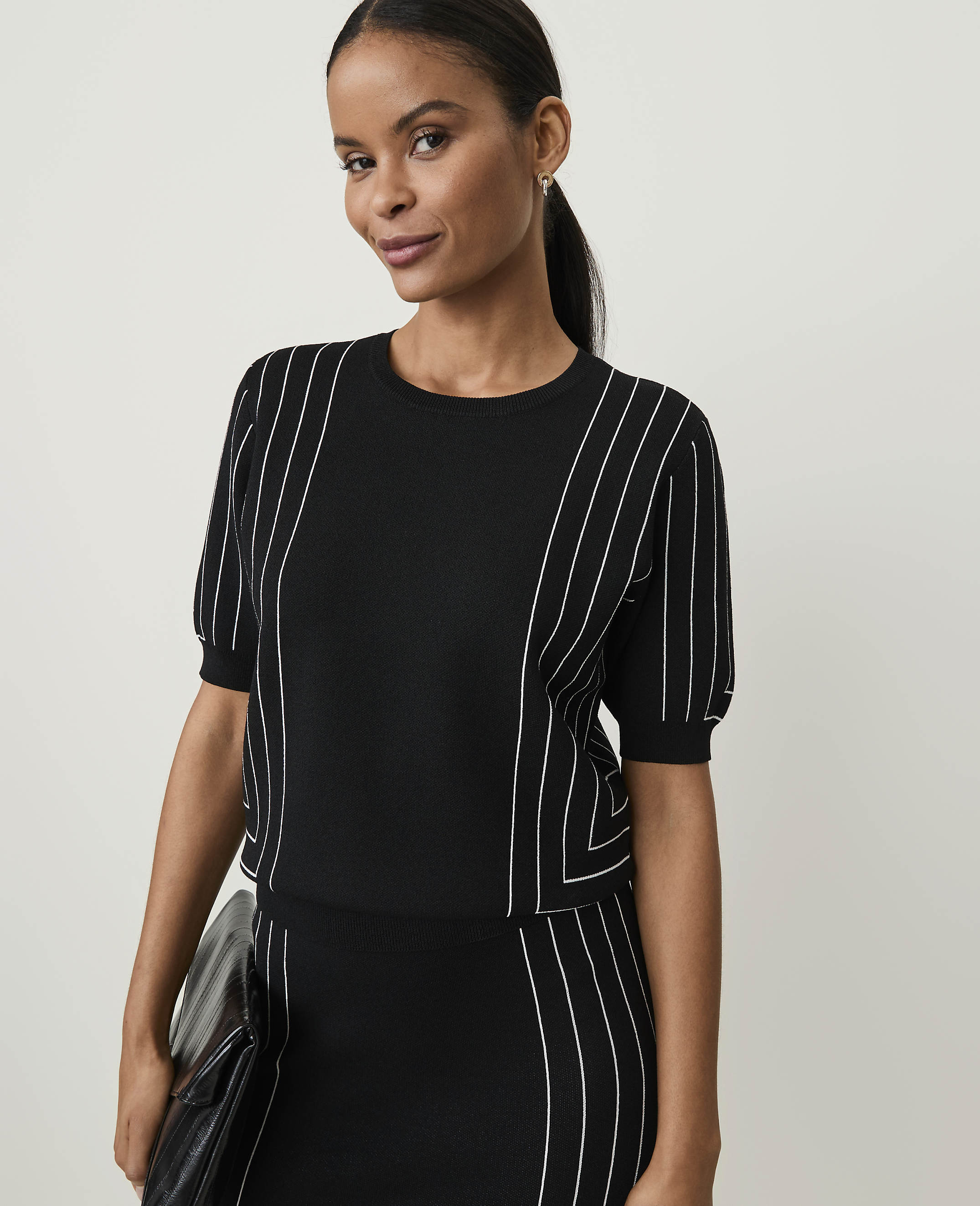 A woman in a black and white striped top and skirt stands against a plain white background.