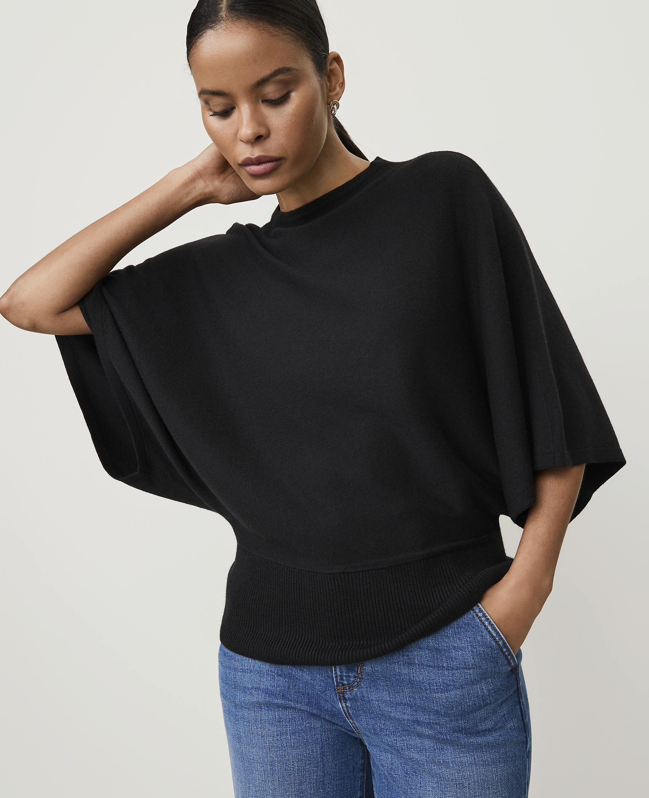 A woman in a black sweater and blue jeans poses against a plain, light background.