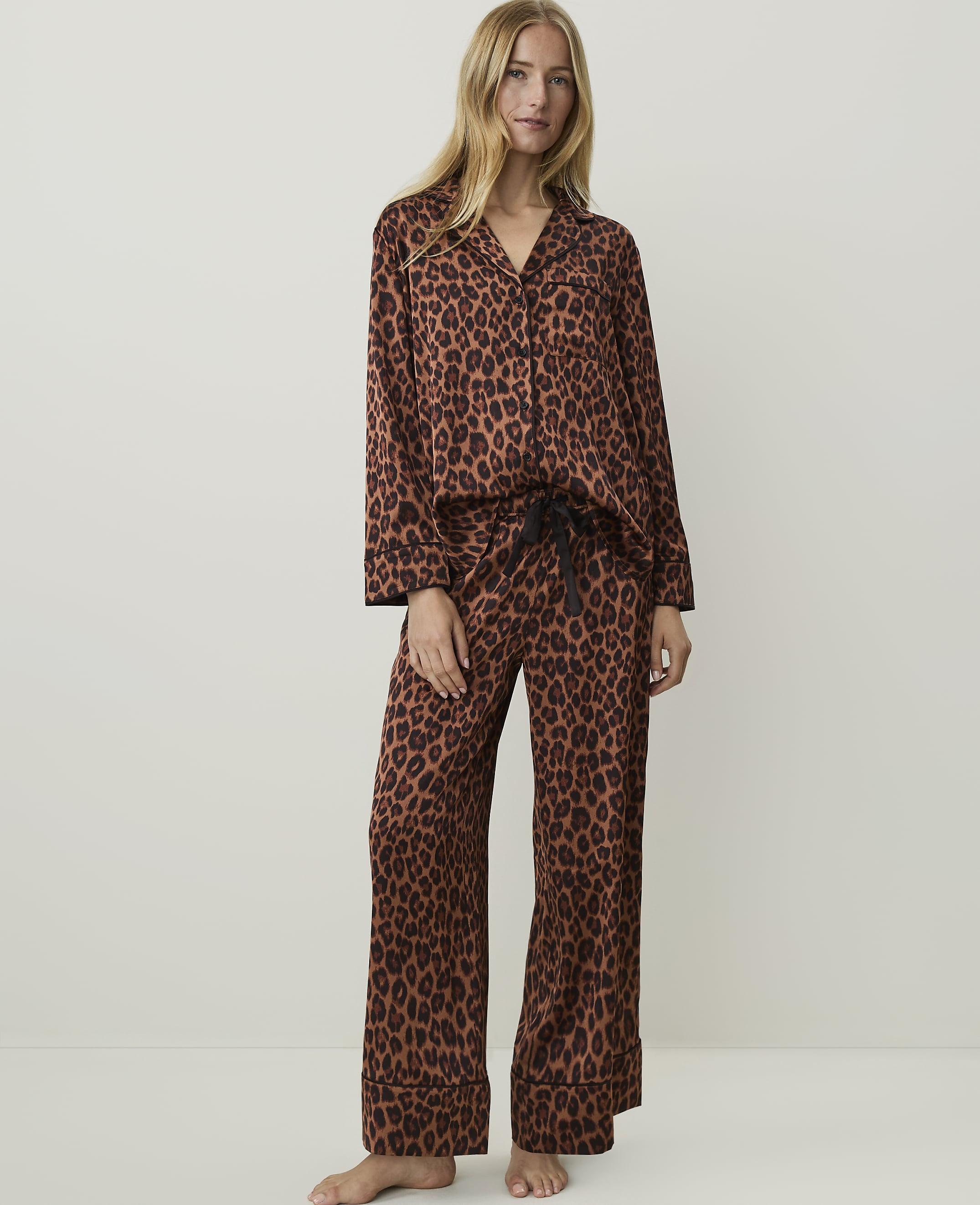 A woman in leopard print pajamas stands against a plain, light-colored background.