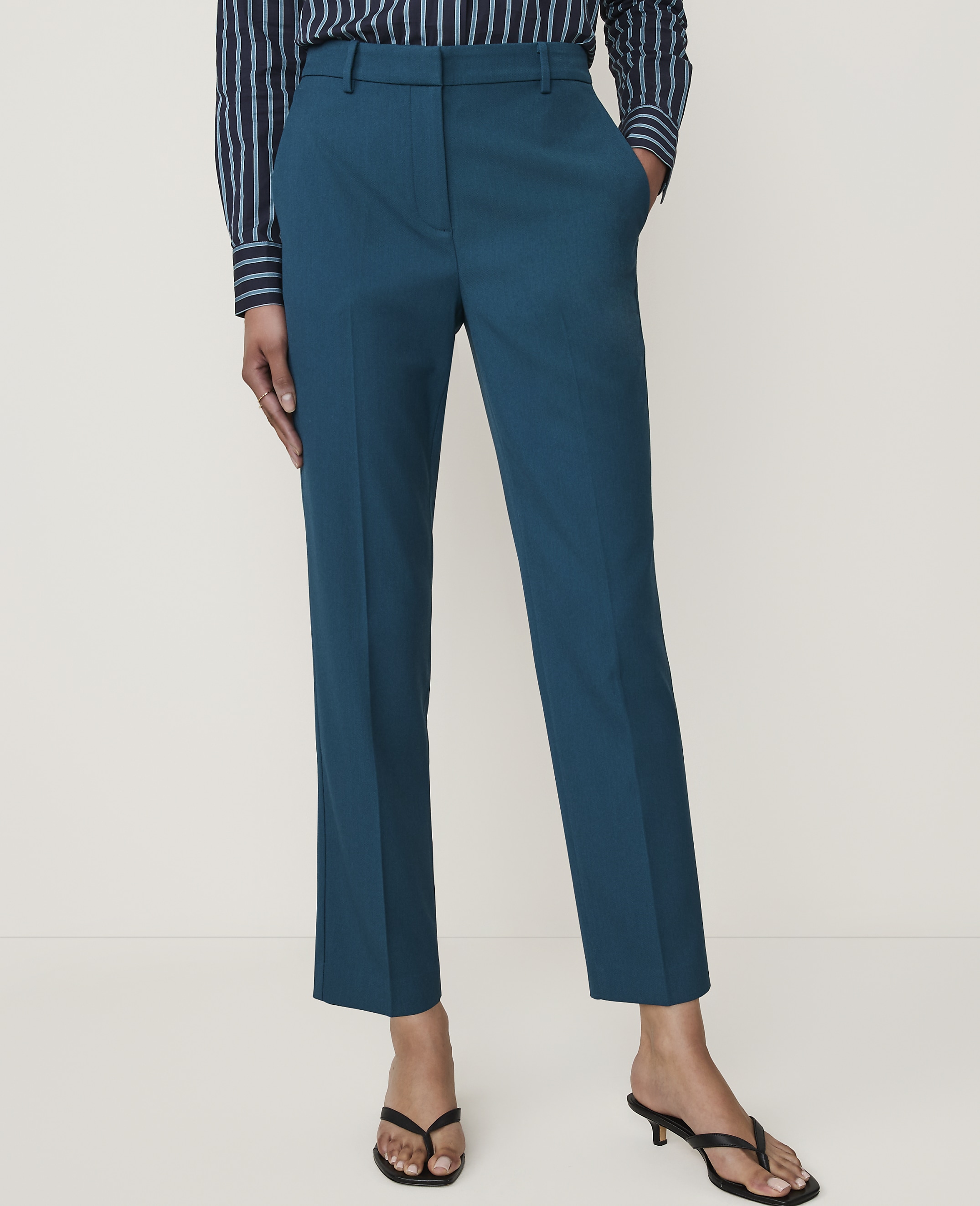 A person stands in teal trousers and a striped shirt against a plain white background.