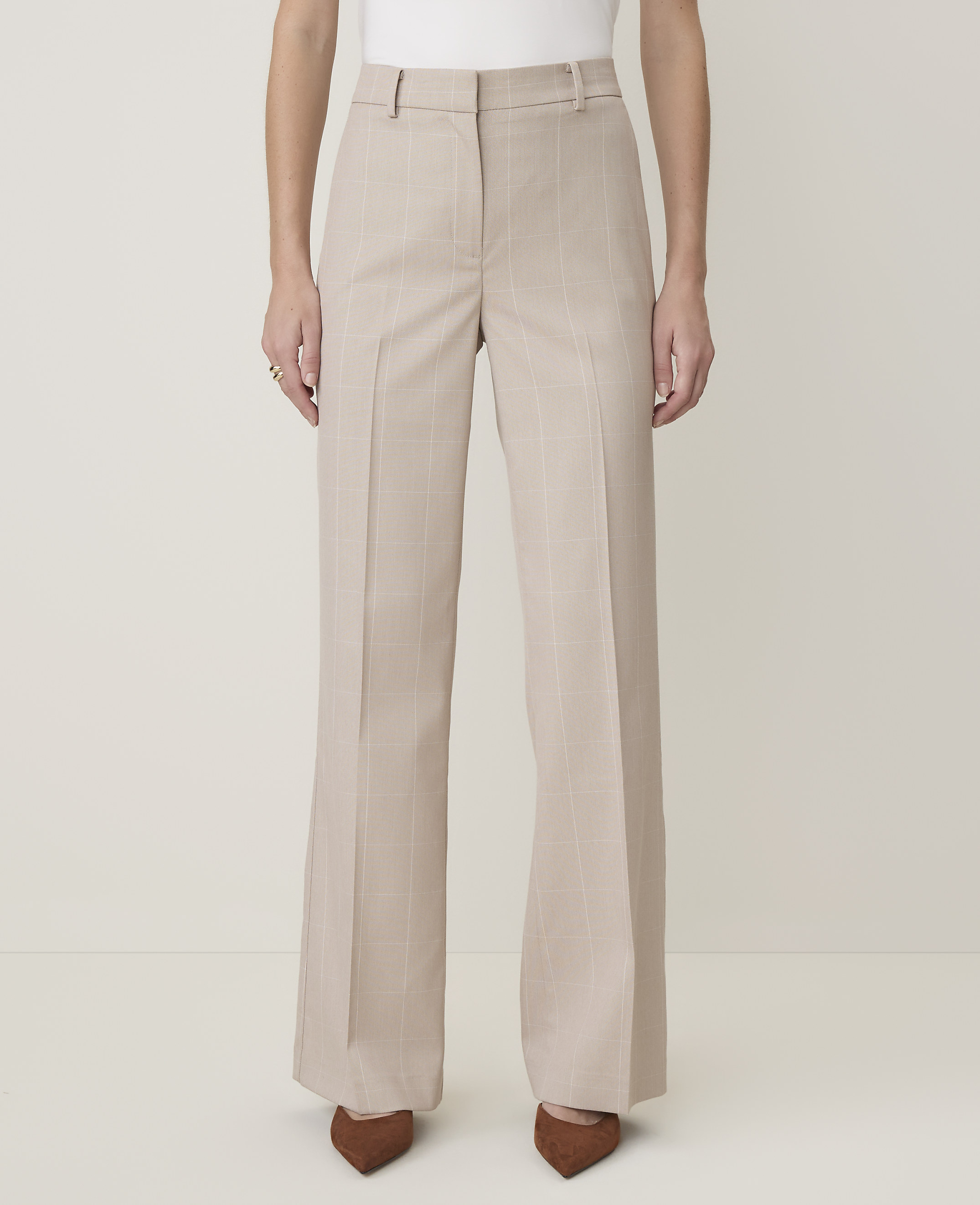 A person stands in light-colored, wide-leg trousers with subtle pinstripes, wearing brown pointed-toe heels against a plain, light background.