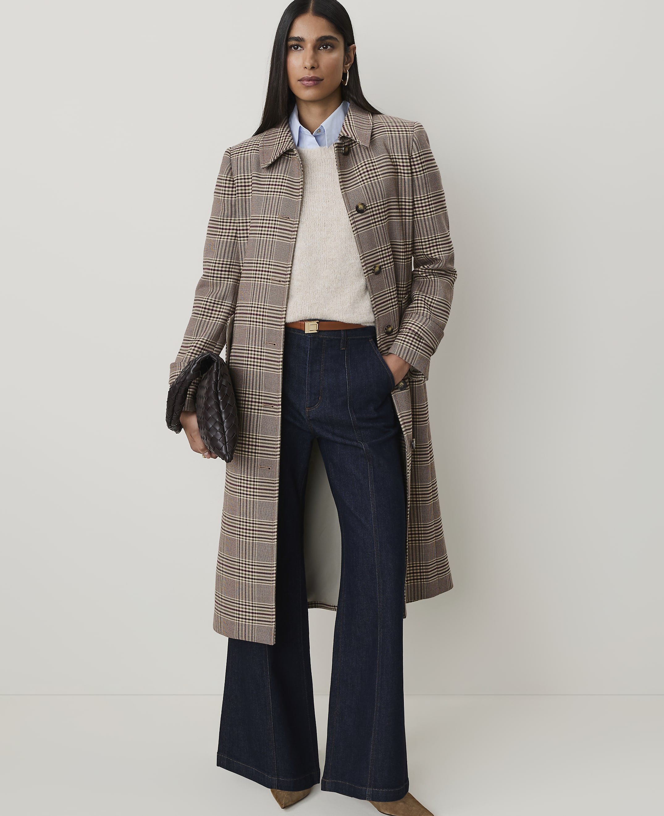 A woman in a plaid coat and wide-leg jeans stands against a plain, light background.