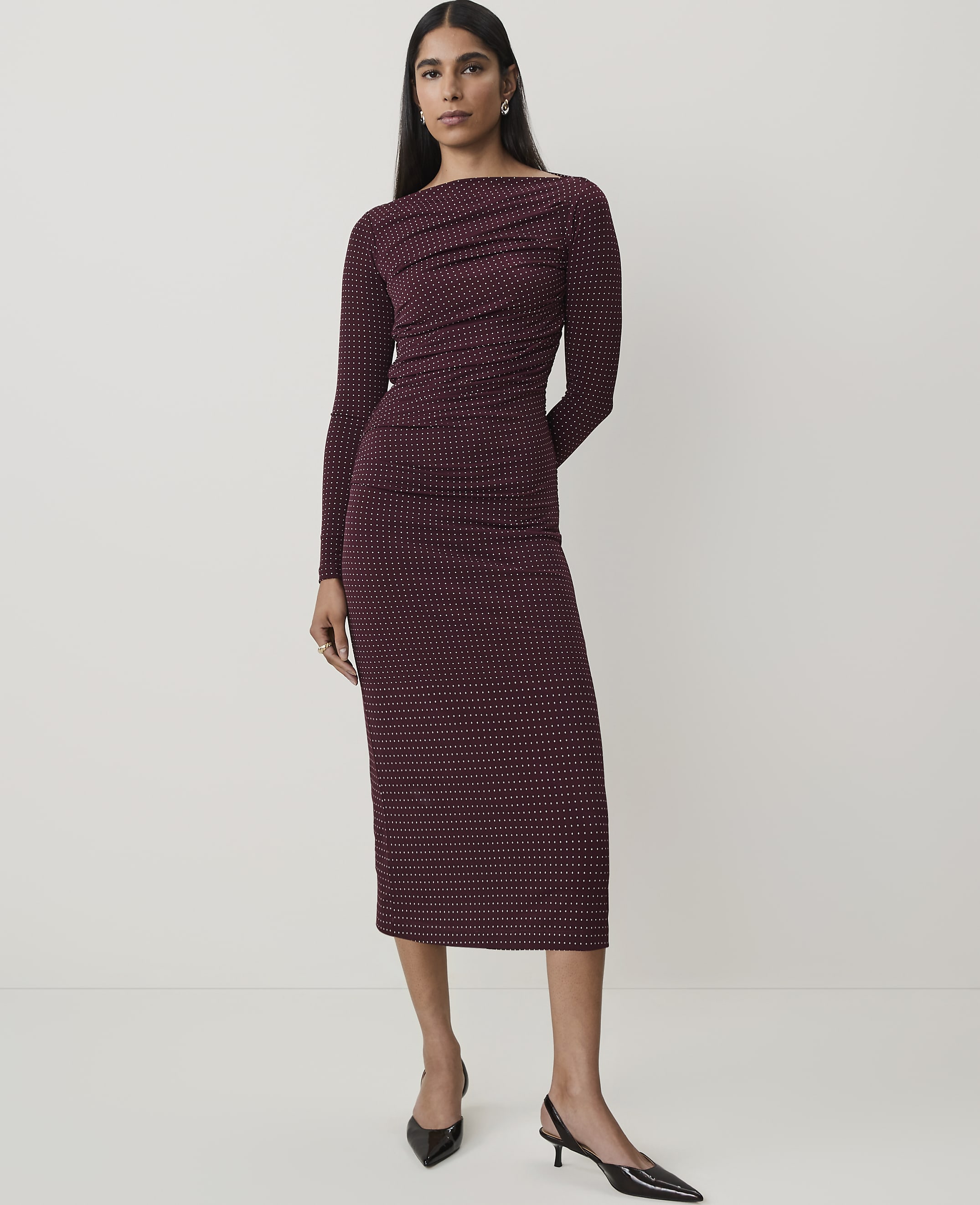 A woman in a patterned maroon dress stands against a plain white background.
