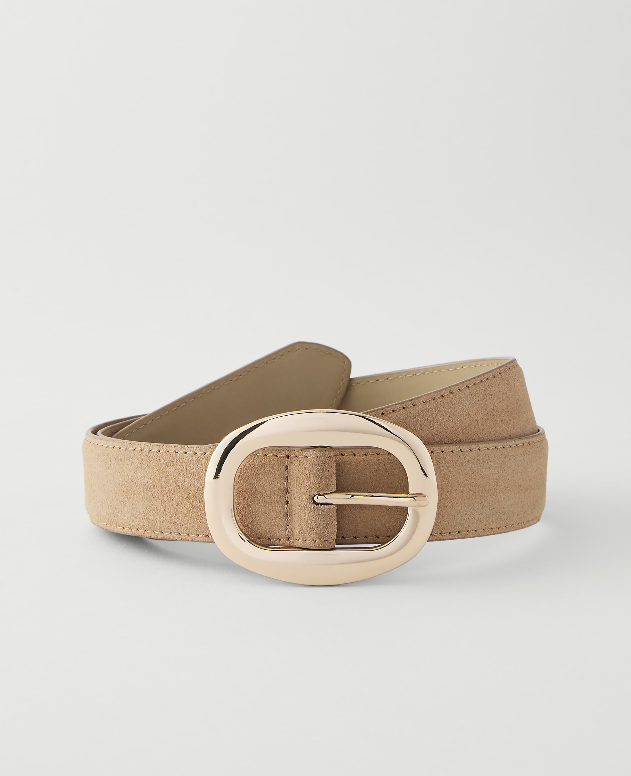 A tan suede belt with a large, oval, rose gold buckle lies on a plain white background.