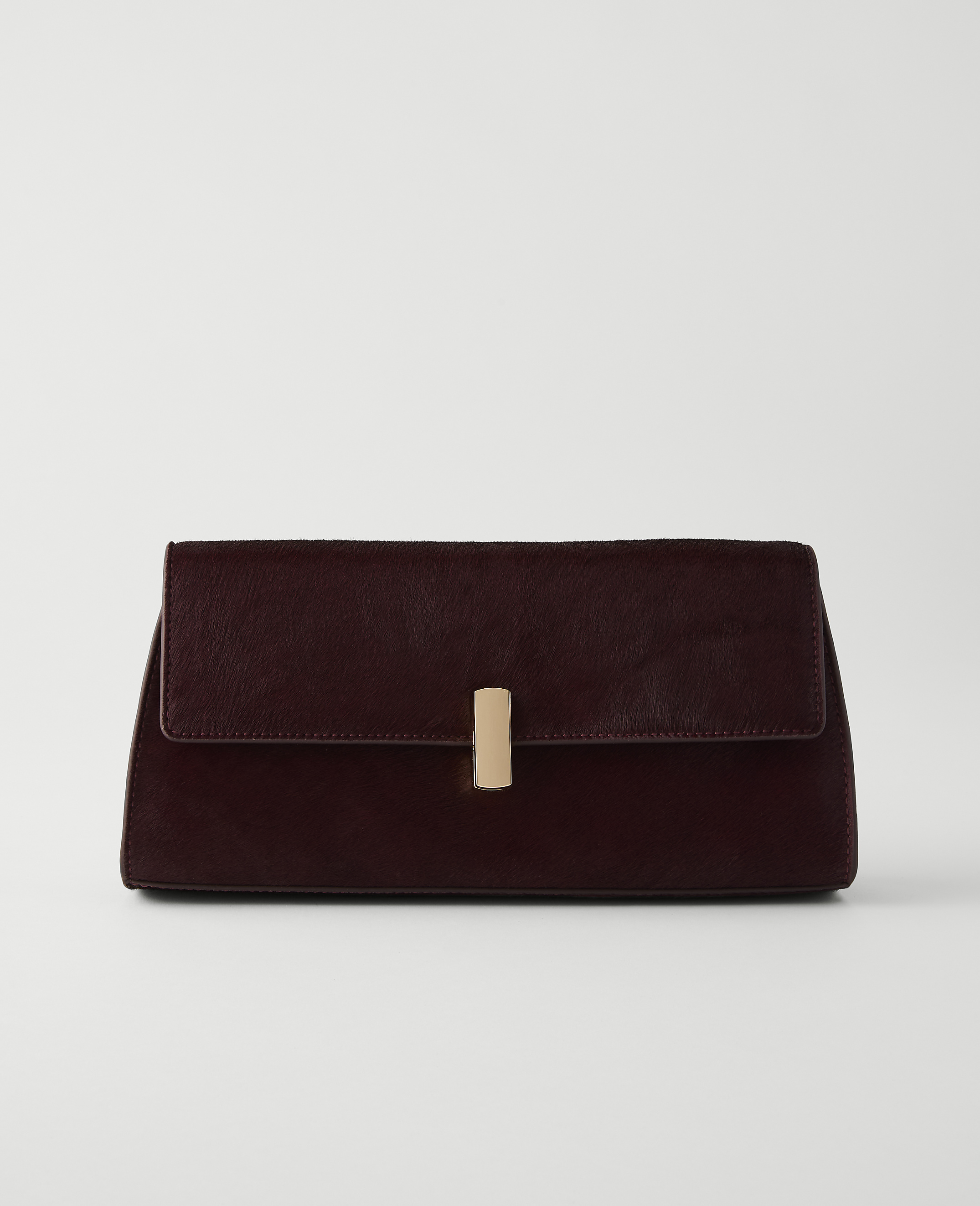 A dark red clutch with a gold clasp rests on a white surface against a plain white background.