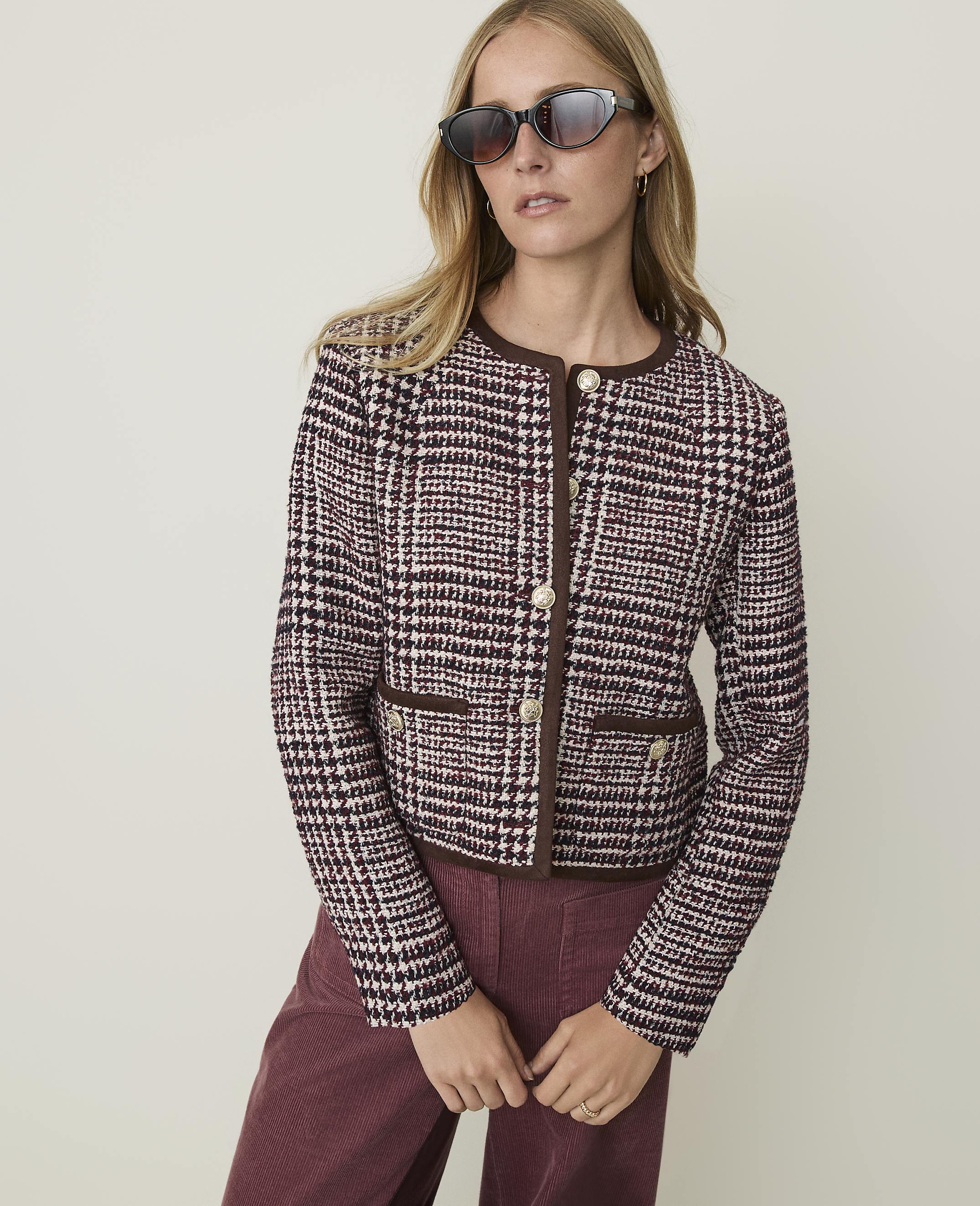 A woman in a tweed jacket and corduroy pants poses against a plain, light-colored background.