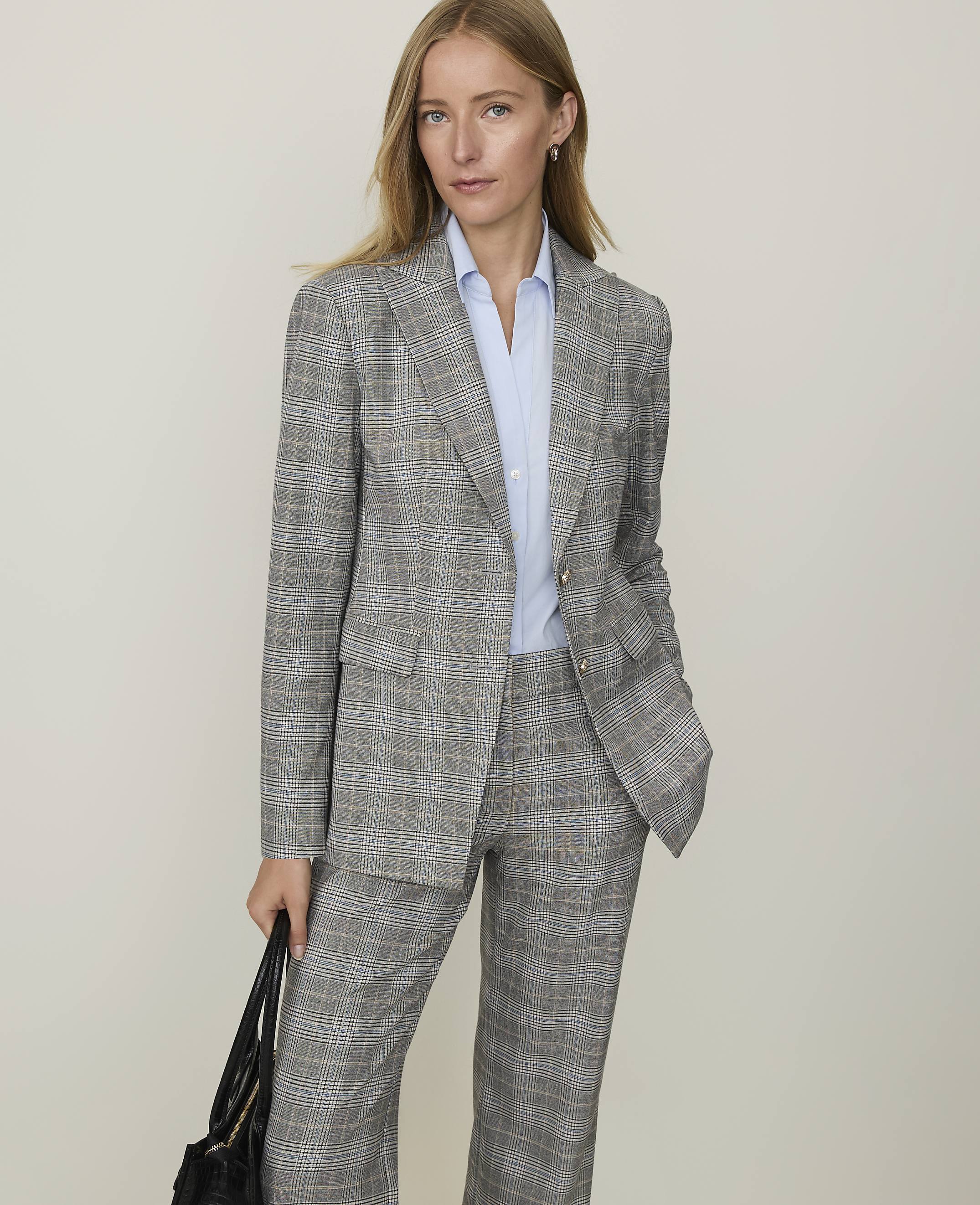 A woman in a plaid suit stands against a plain, light-colored background.