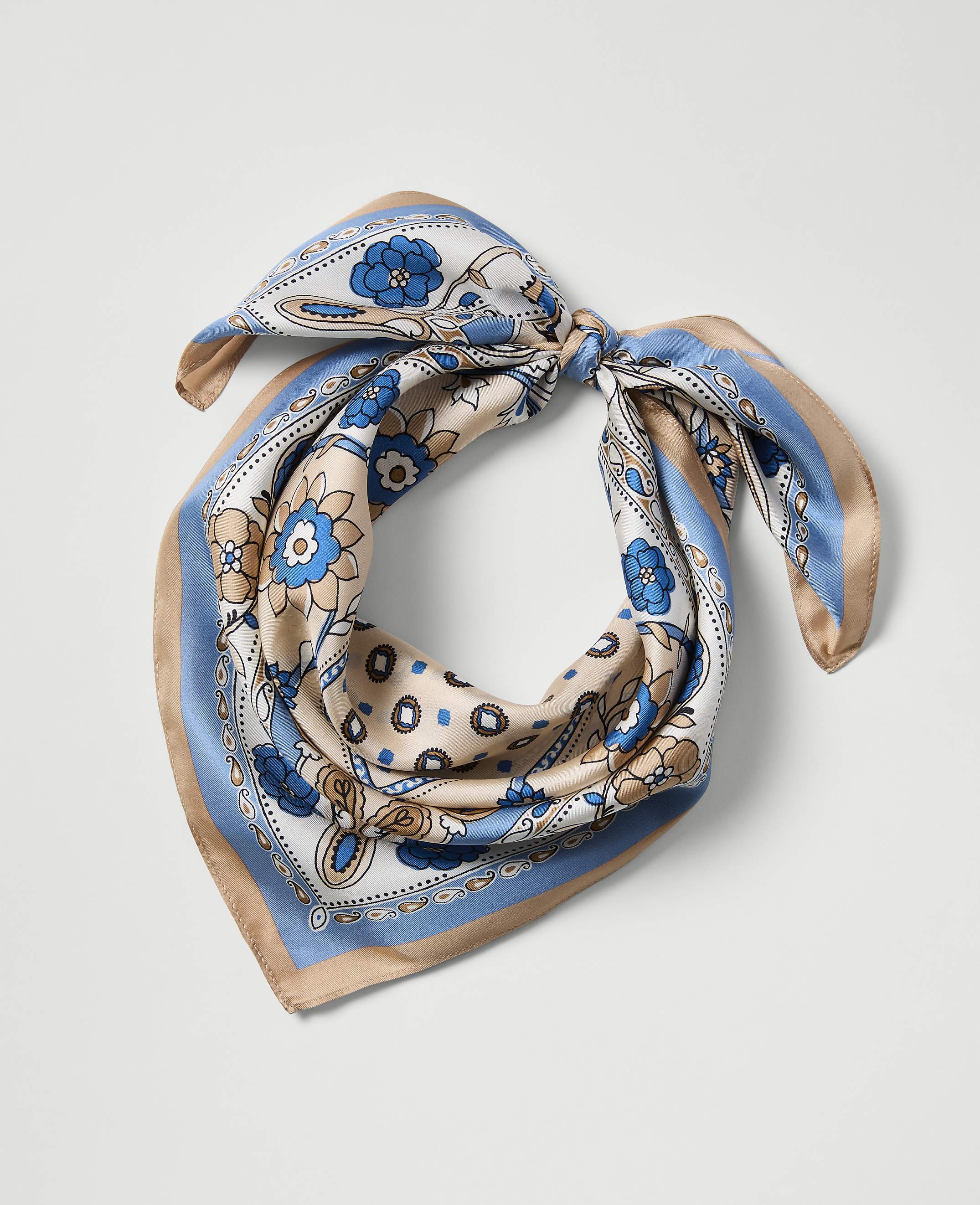 A patterned silk scarf with blue and tan floral designs is tied in a knot against a plain white background.