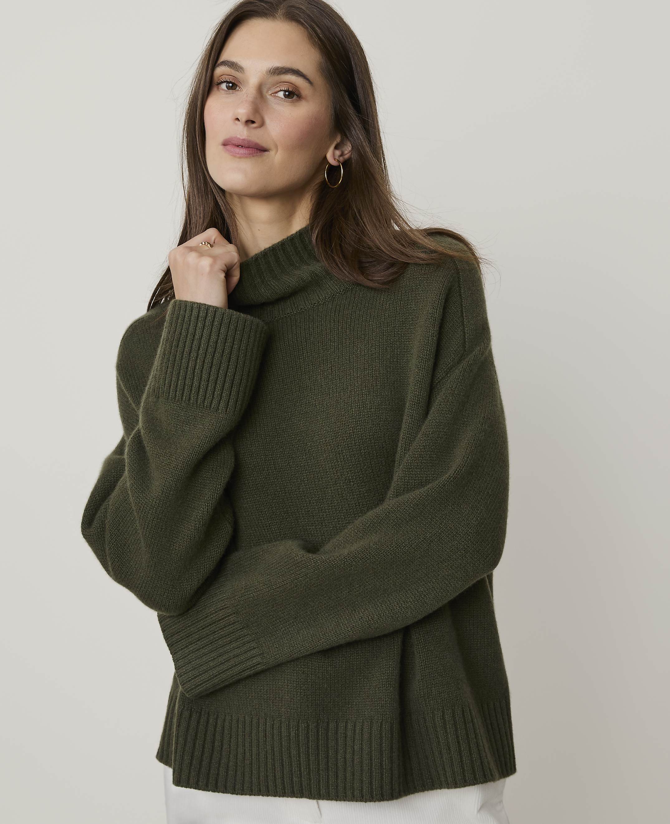 A woman in a green turtleneck sweater poses against a plain, light-colored background.