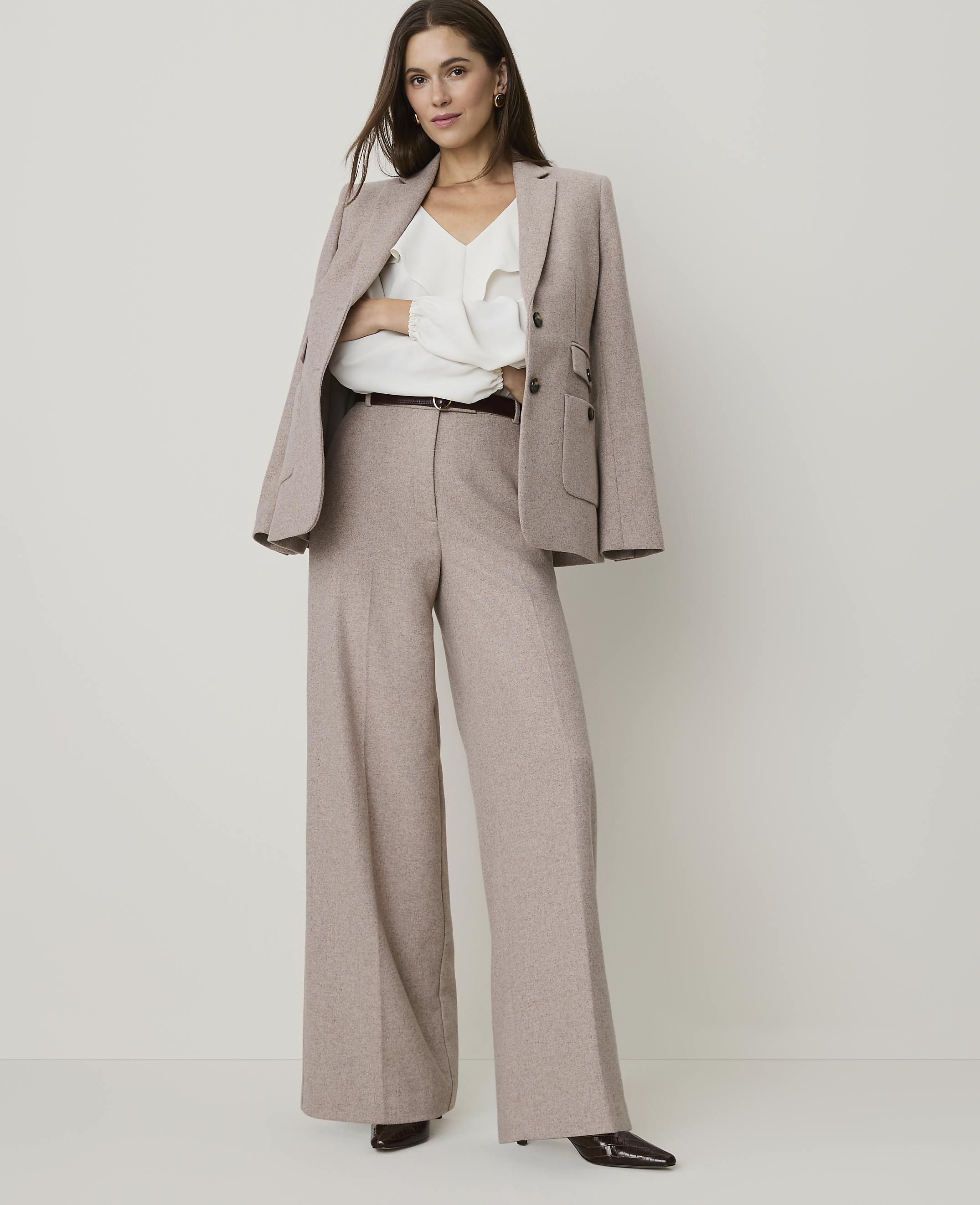 A woman in a beige pantsuit stands against a plain white background.