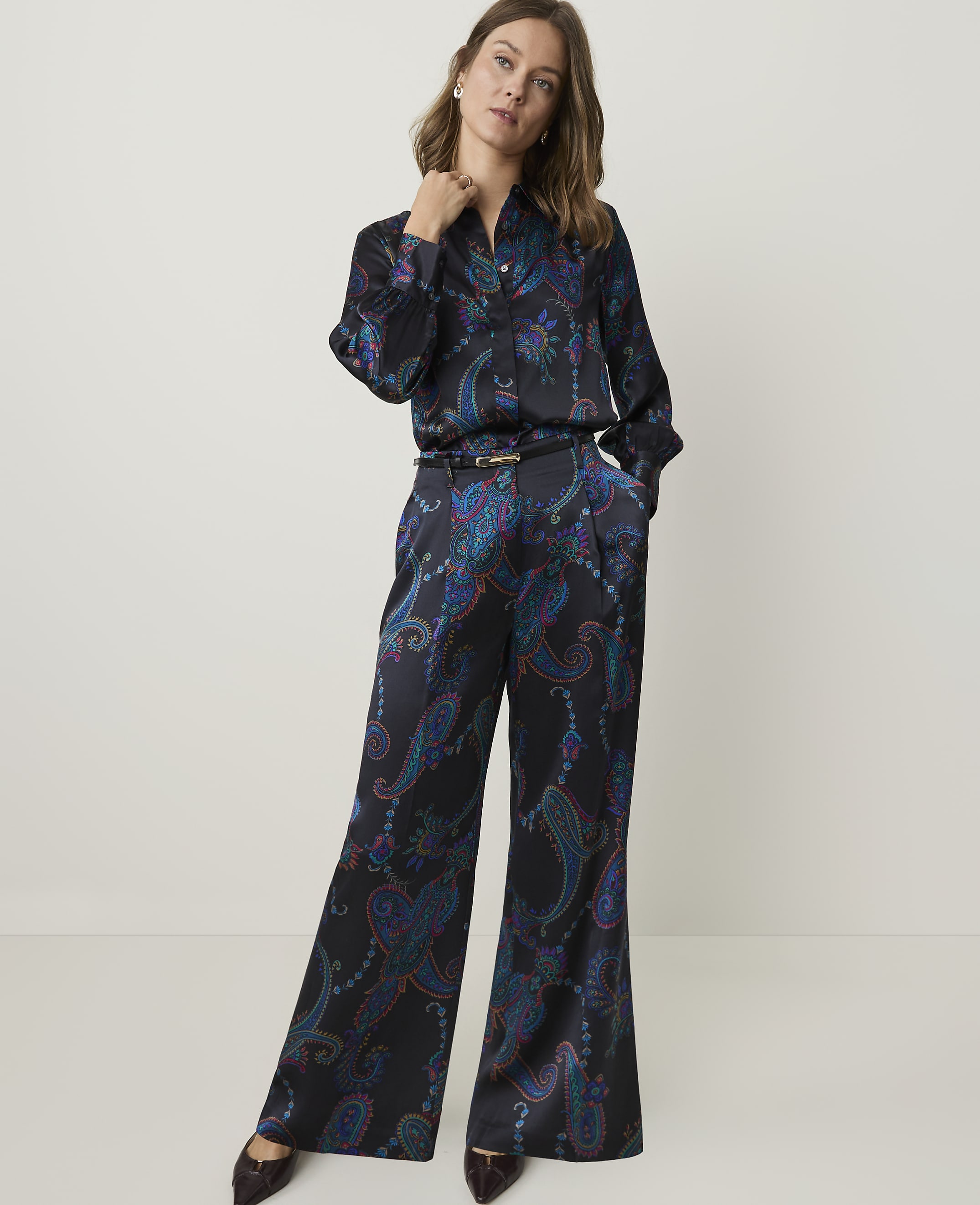 A woman in a patterned silk pajama set stands against a plain, light gray background.