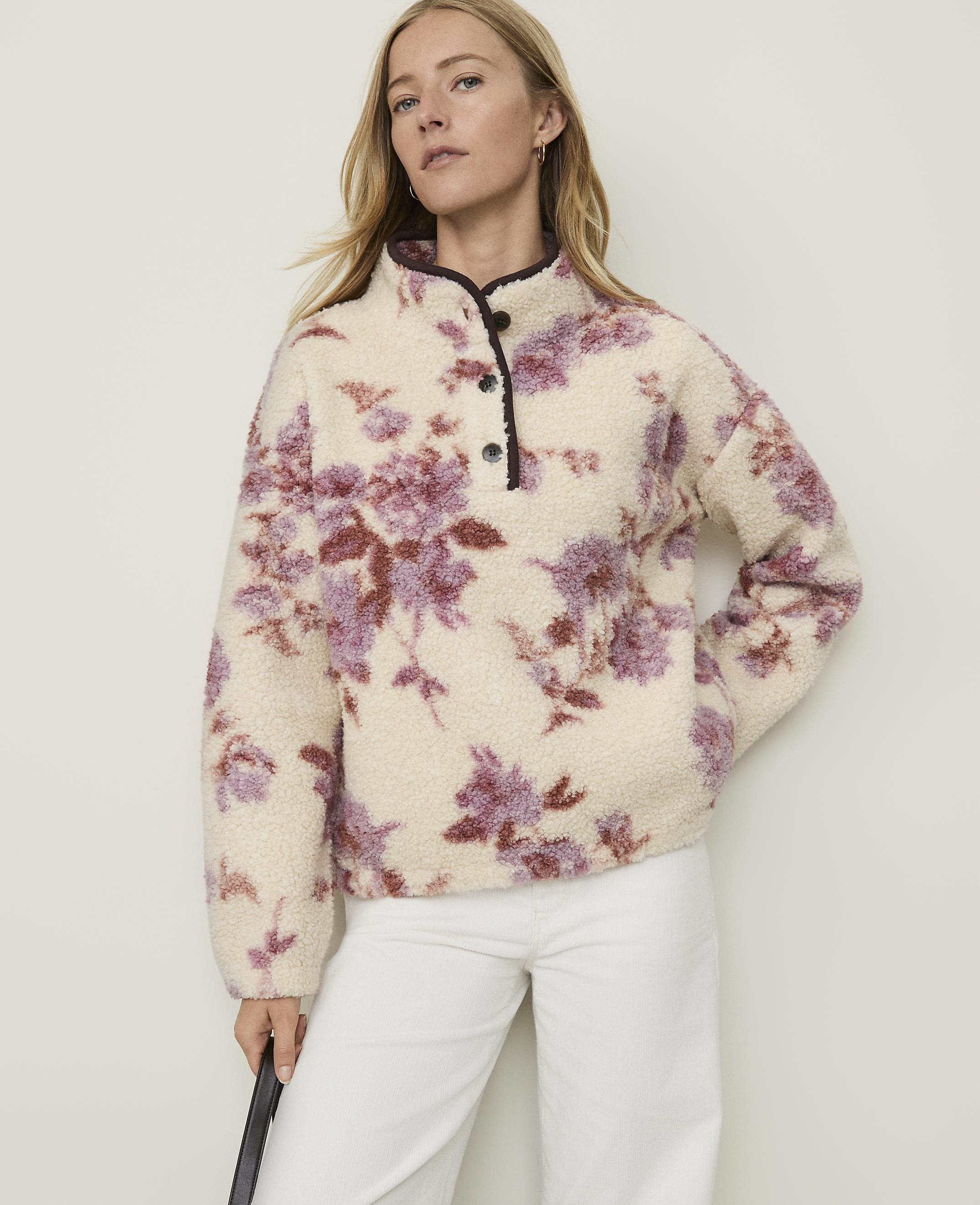 A woman in a cream-colored floral fleece pullover stands against a plain, light-colored background.