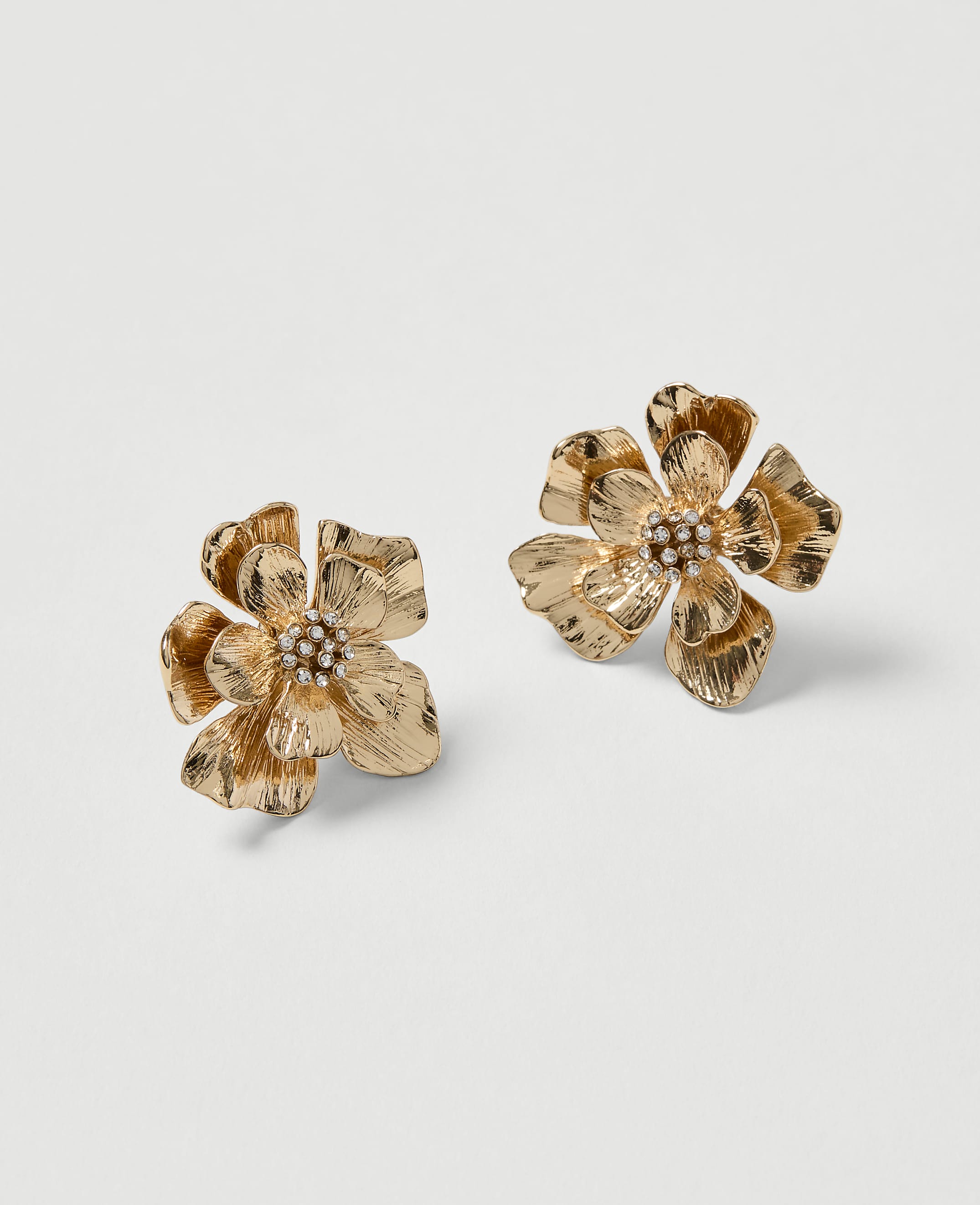 Two golden floral earrings with pearl centers rest on a plain white background.
