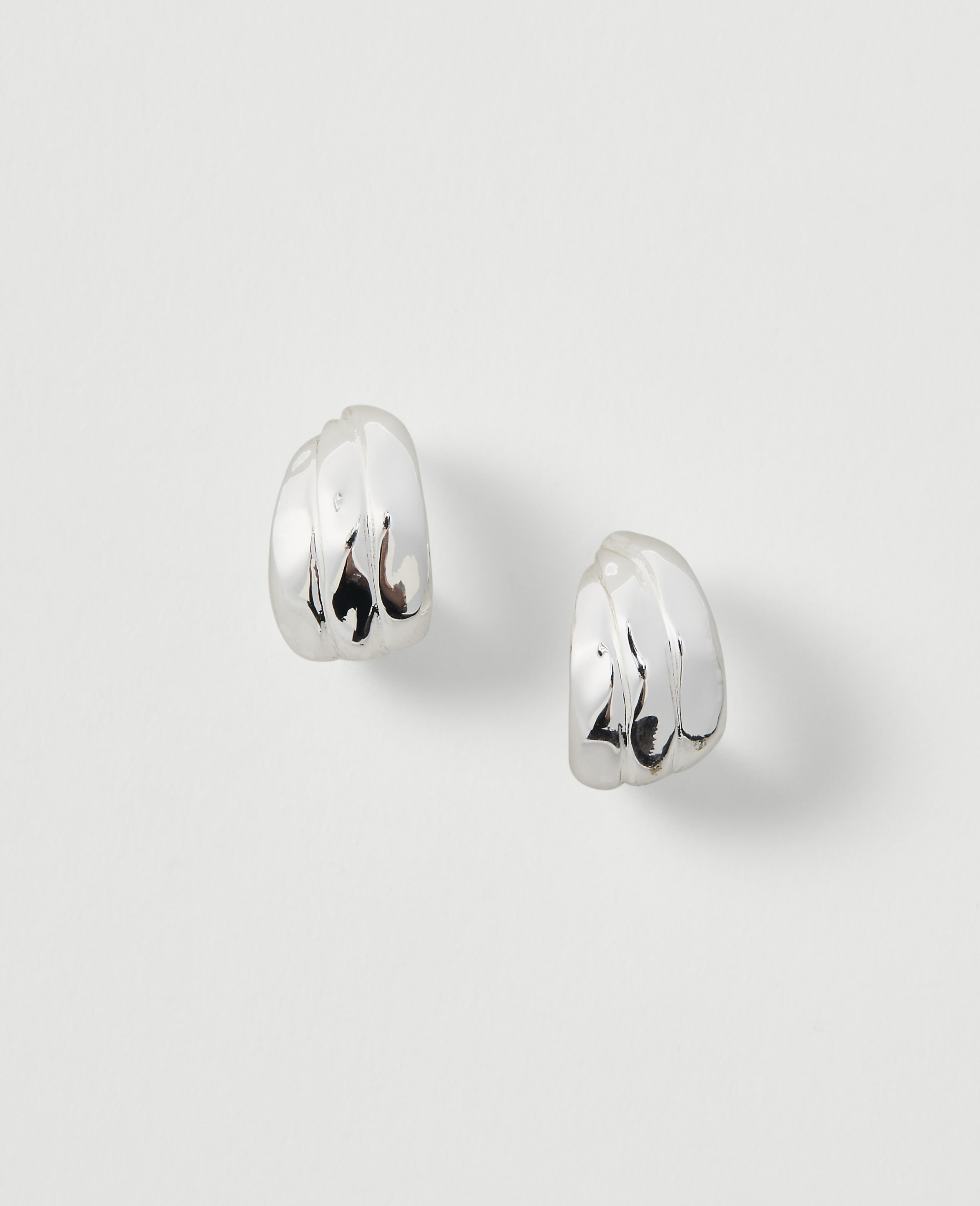 Two silver, ribbed hoop earrings rest on a plain, light gray background.