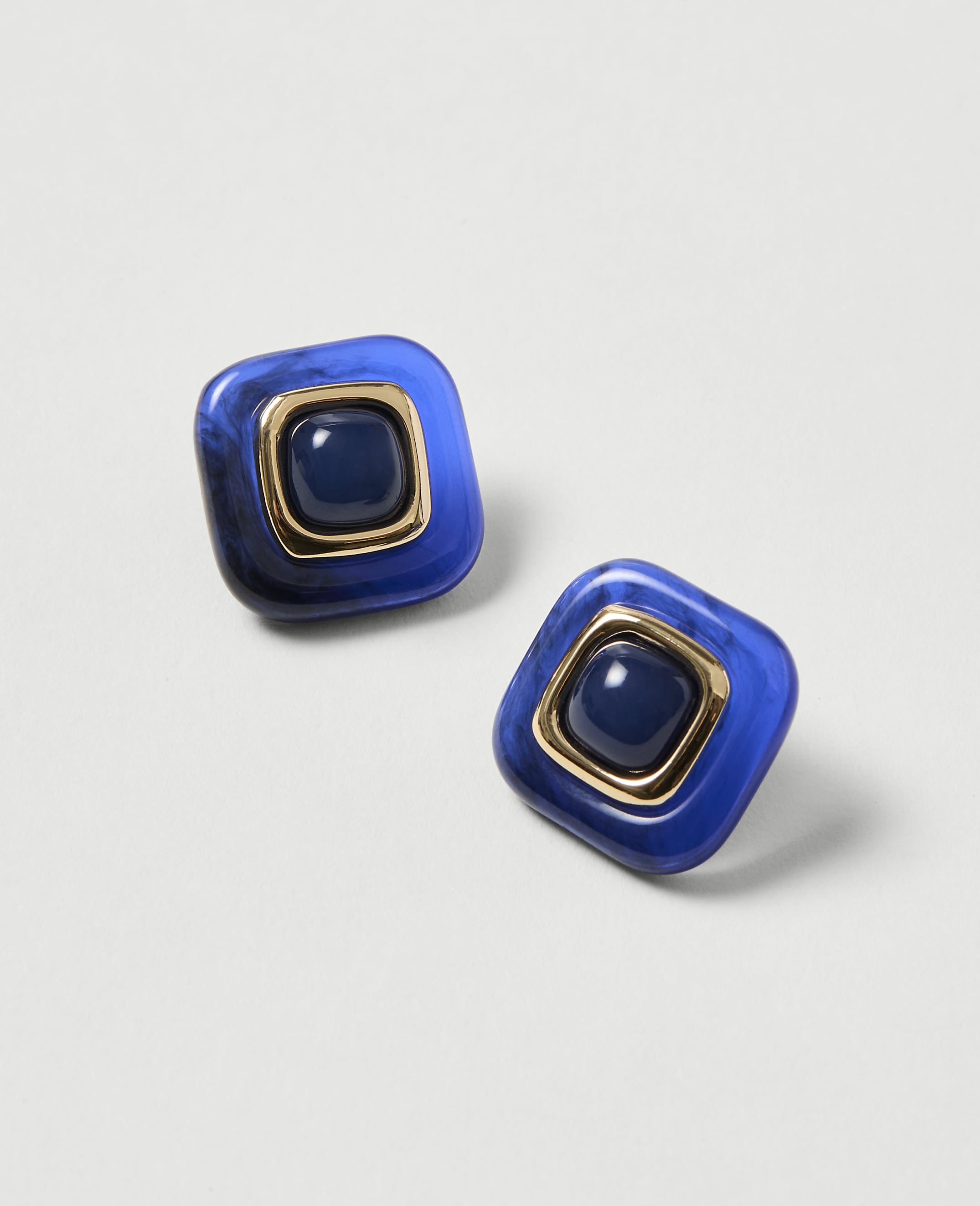 Two square blue earrings with gold trim and a dark blue center stone rest on a light gray background.