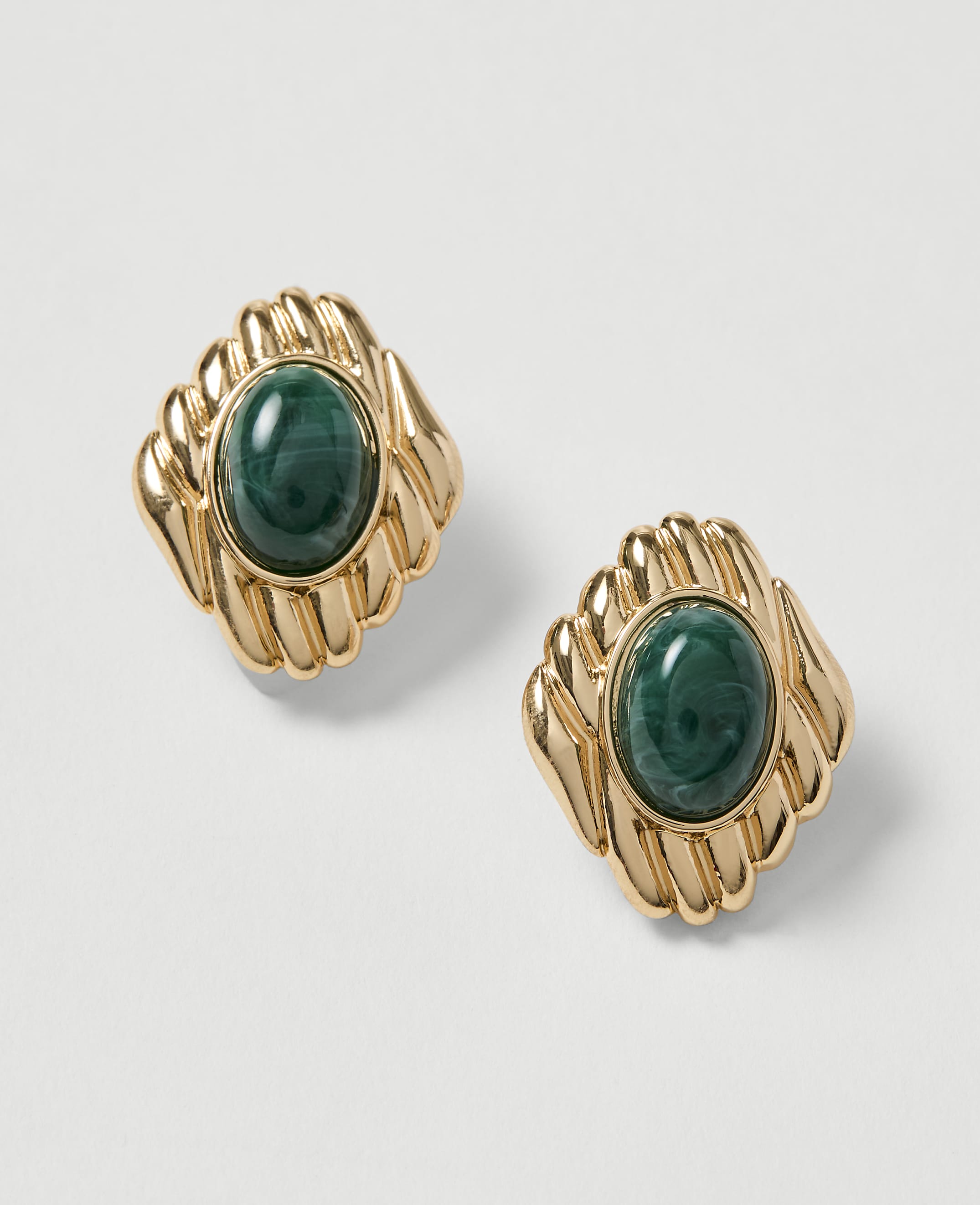 A pair of gold earrings with oval green stones are displayed against a plain white background.