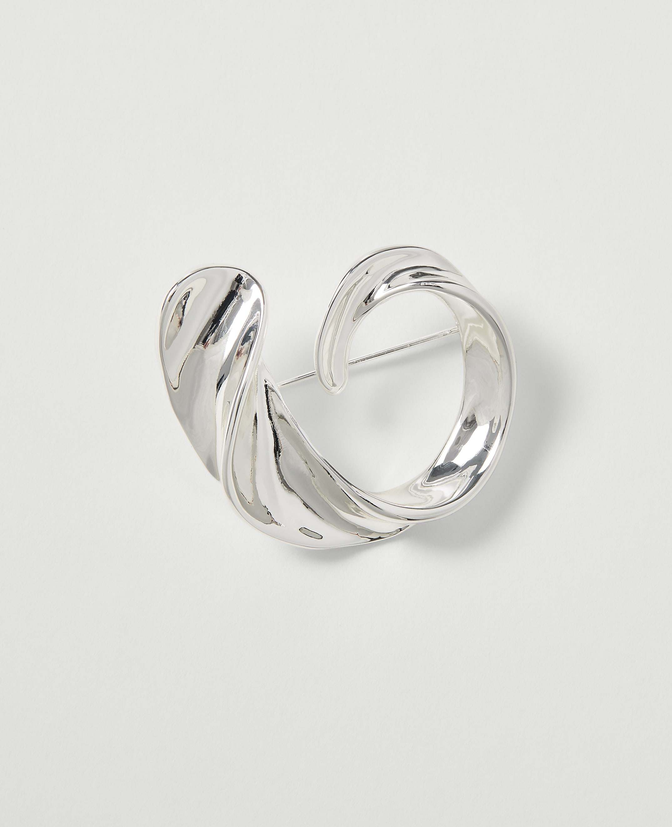 A silver, abstractly shaped brooch with a pin is centered on a plain white background.