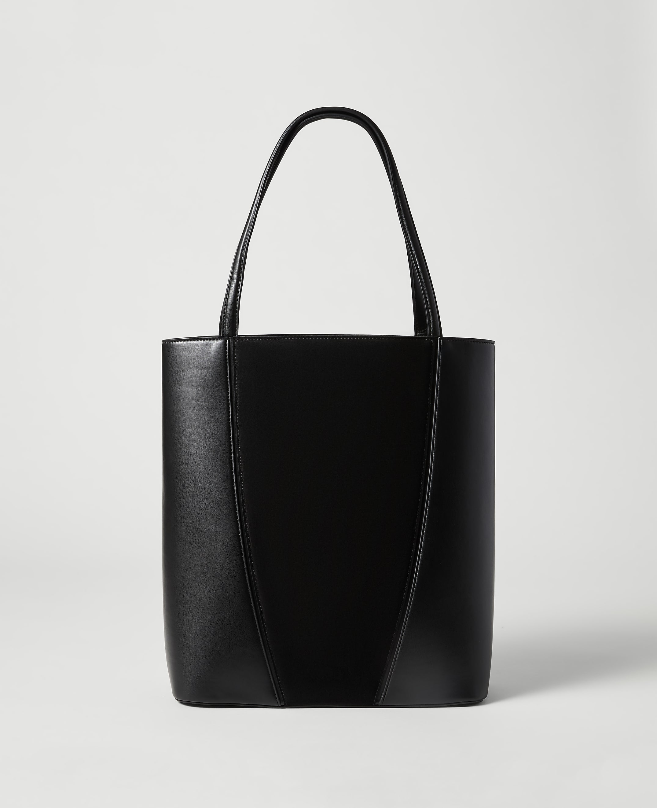 A sleek black leather tote bag with a V-shaped seam stands against a plain, light gray background.