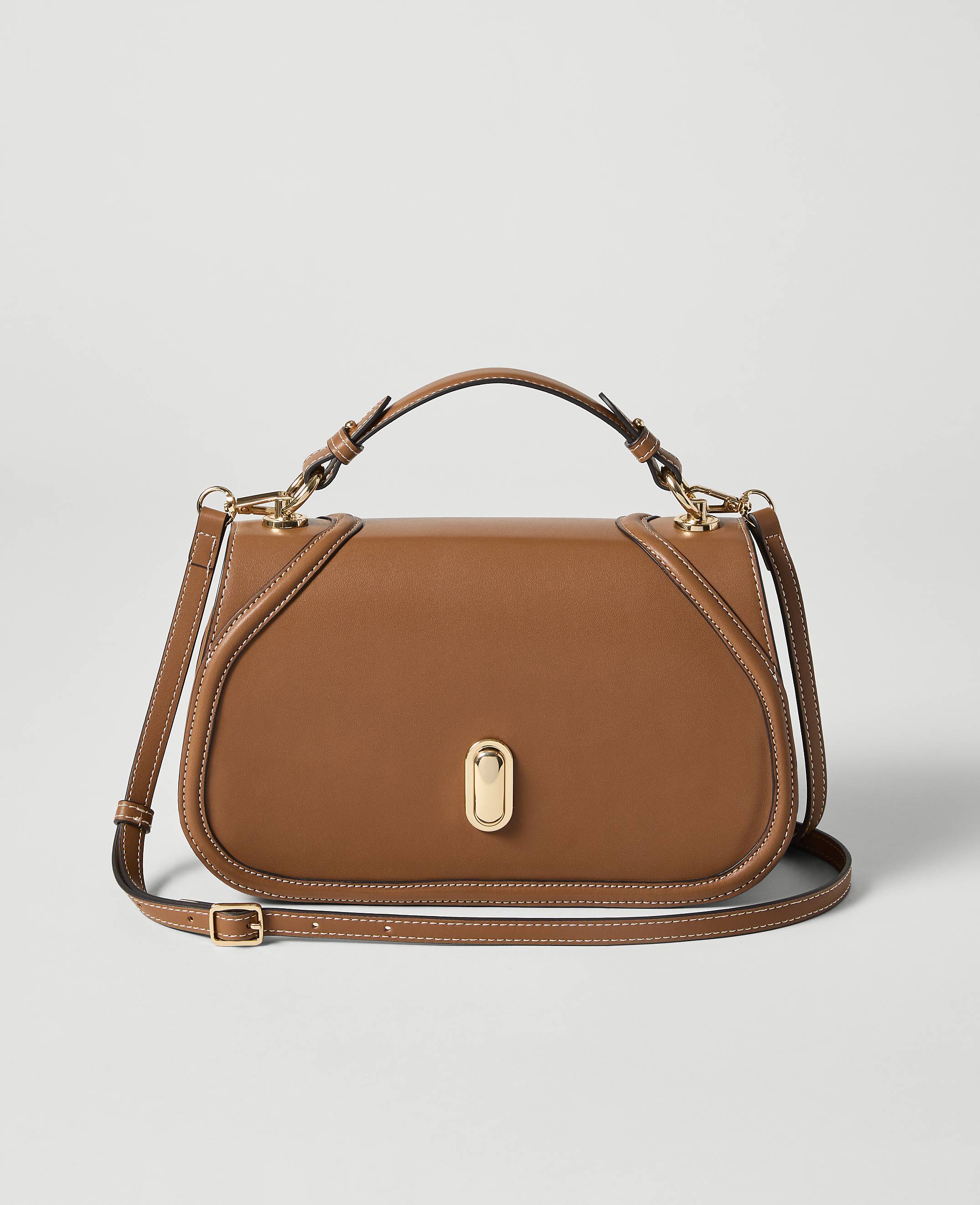 A brown leather handbag with a gold clasp sits in the foreground against a plain, light gray background.