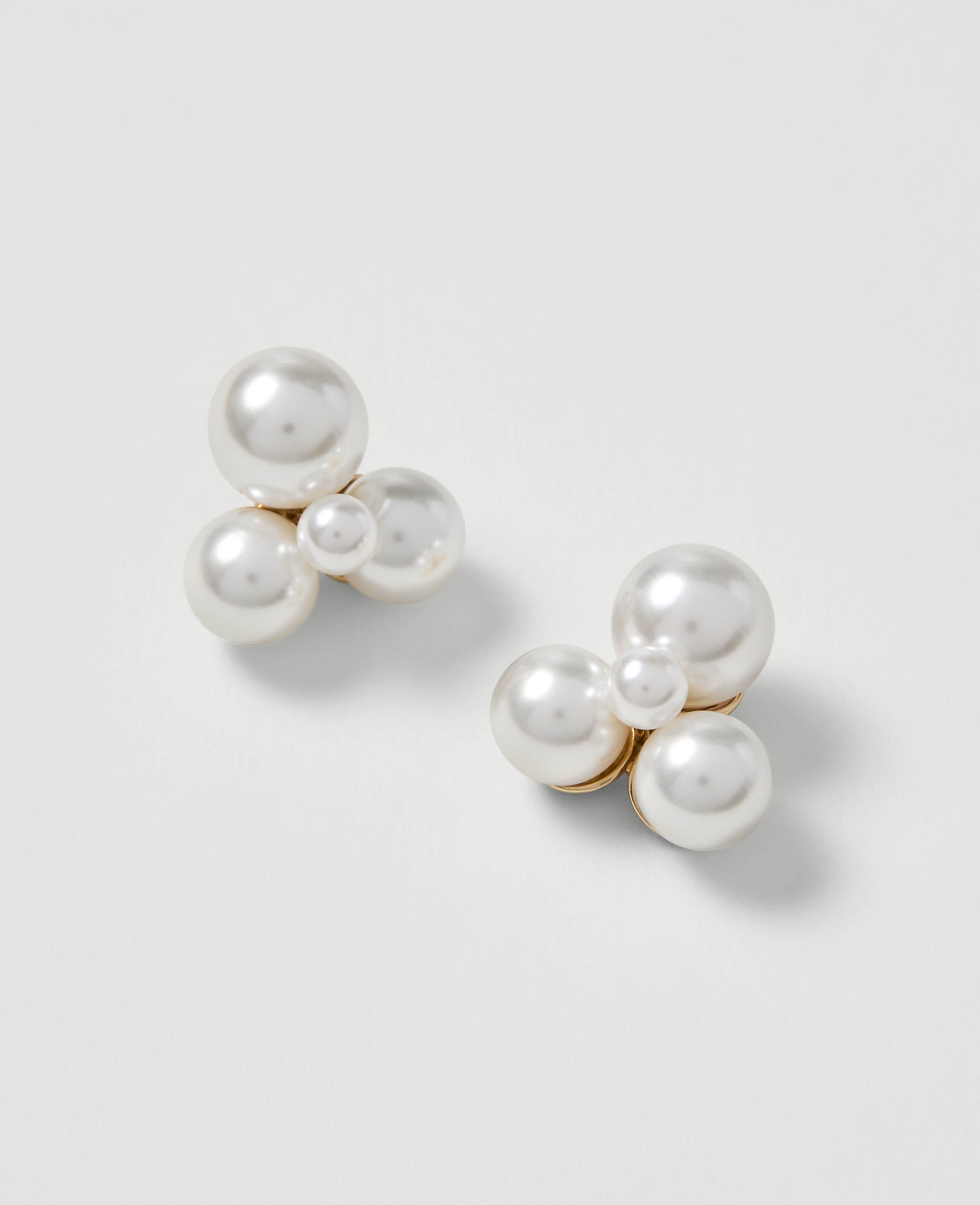 A cluster of pearl earrings rests on a plain white background.