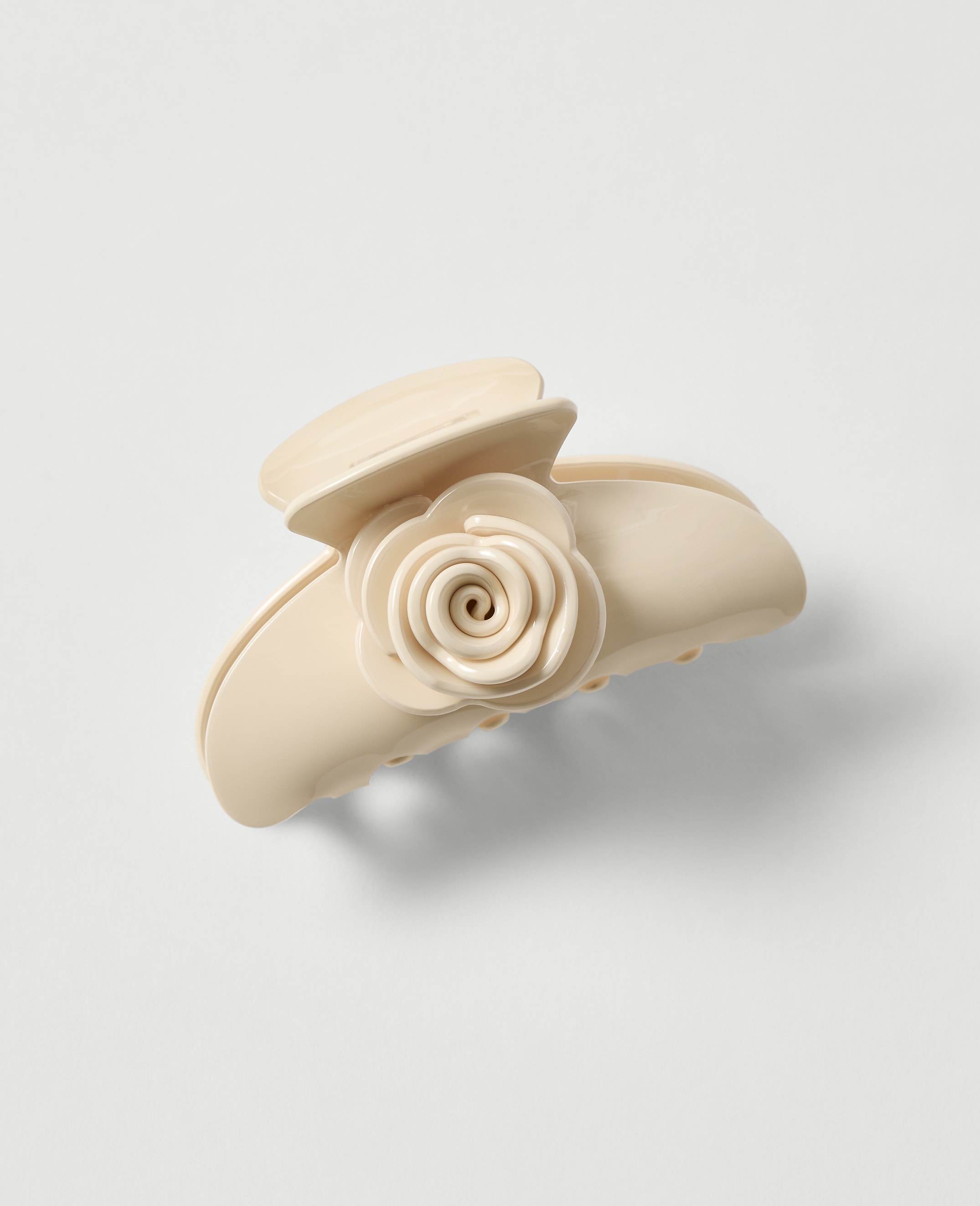 A cream-colored claw clip with a rose embellishment rests on a plain, light gray background.
