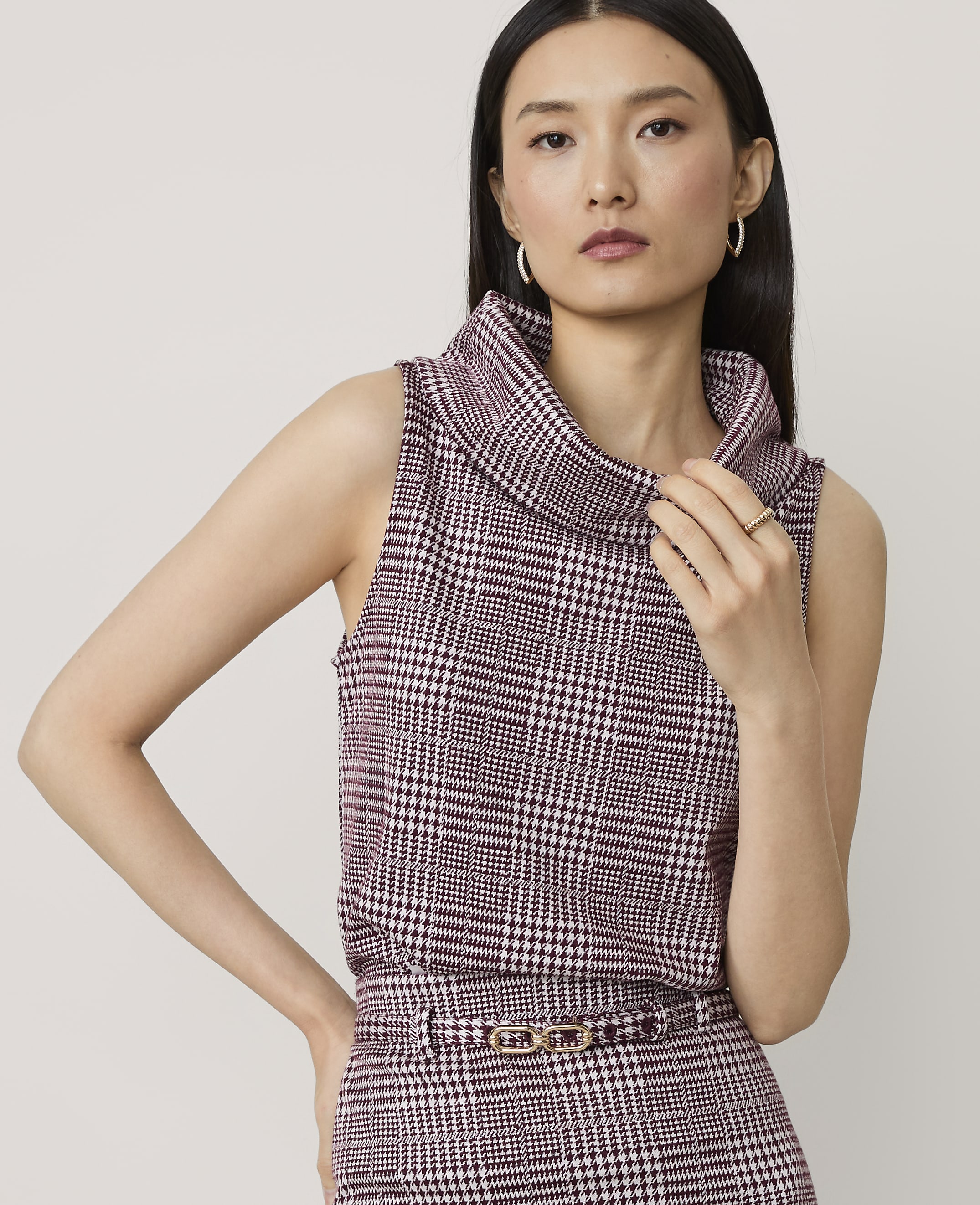 A woman in a plaid cowl-neck top and skirt stands against a plain background.