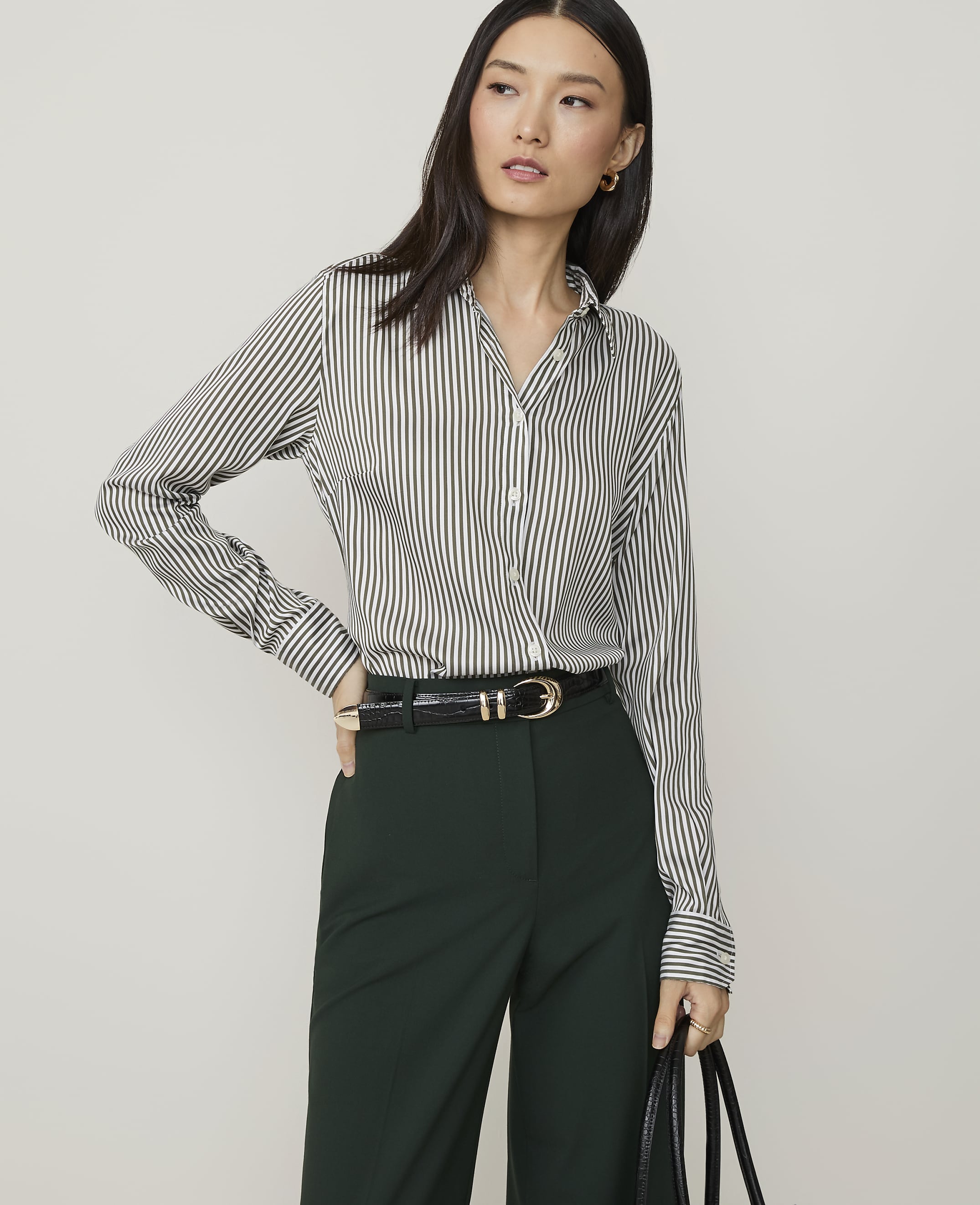 A woman in a striped shirt and brown suede skirt stands against a plain white background.