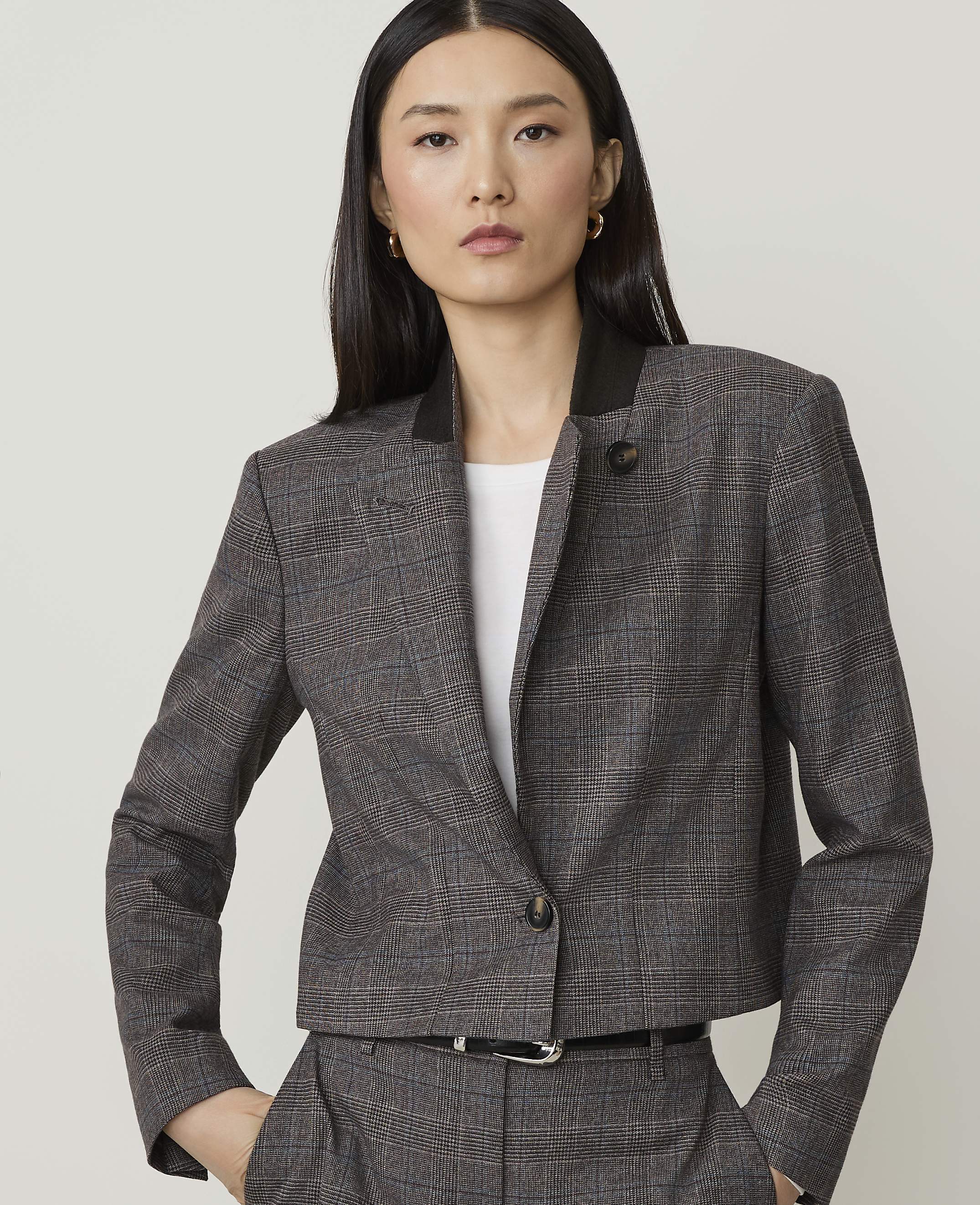 A woman in a plaid jacket and pants stands against a plain, light gray background.