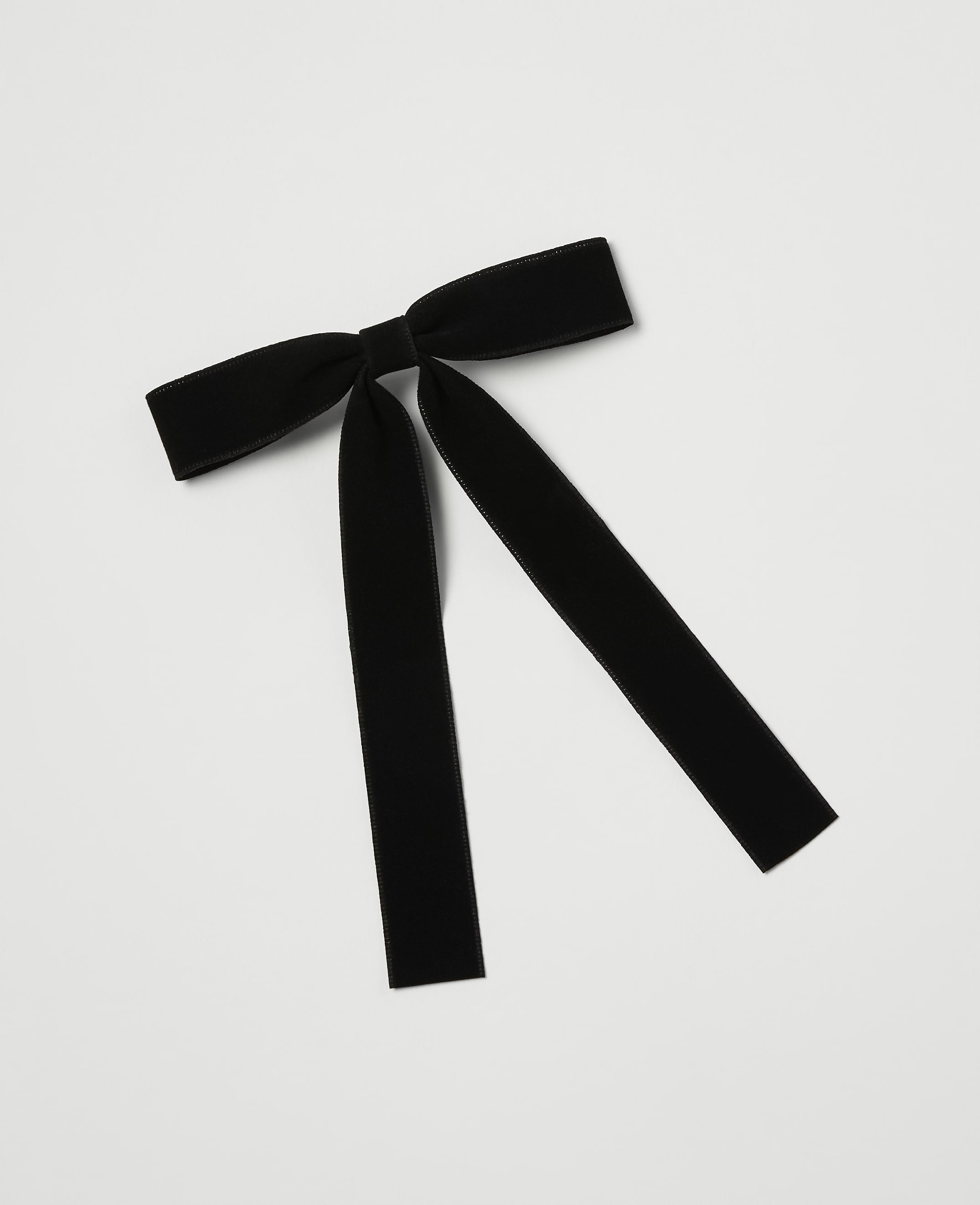 A black velvet bow with long, trailing ribbons lies on a plain white background.