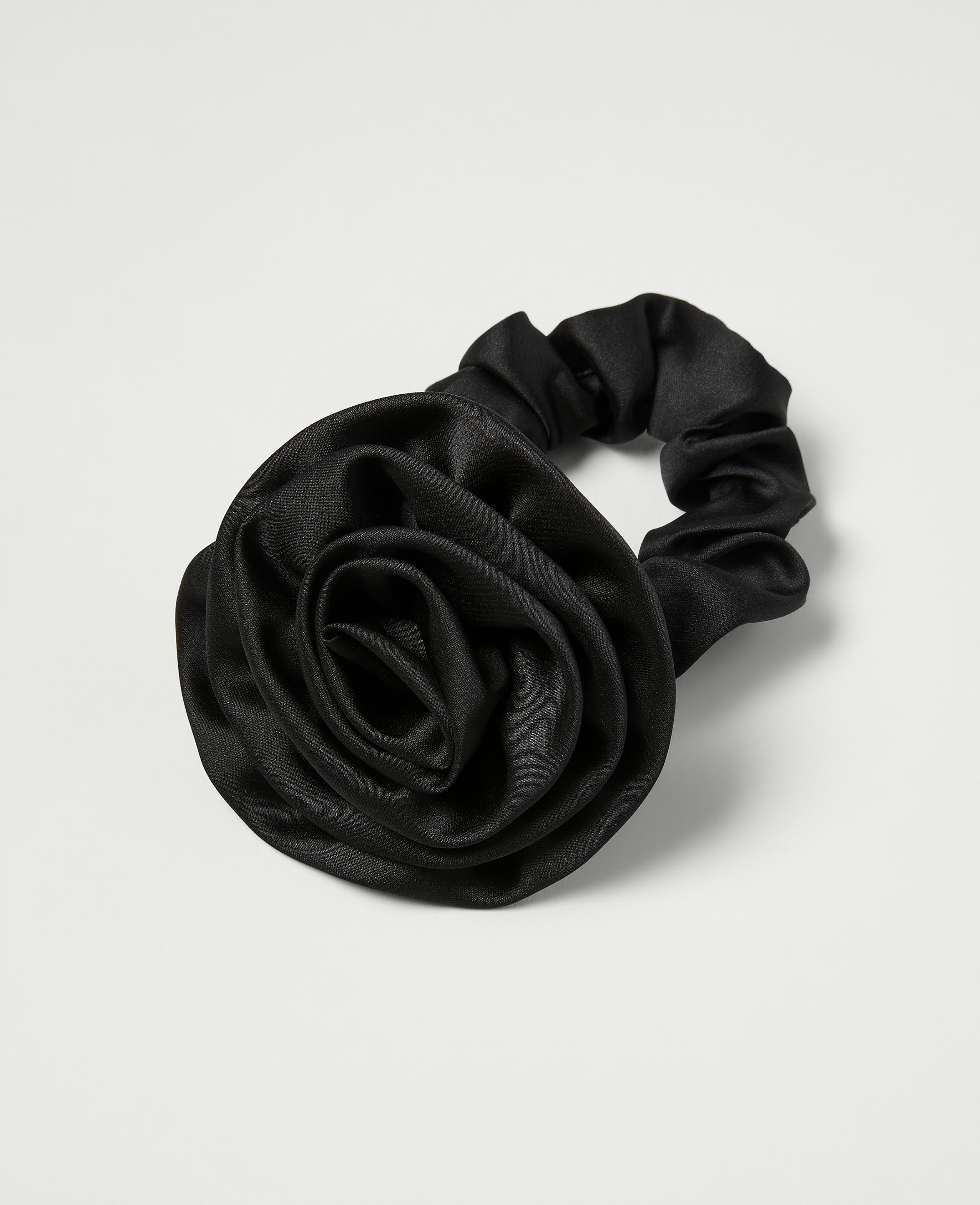 A black satin scrunchie with a rose embellishment rests on a plain white background.